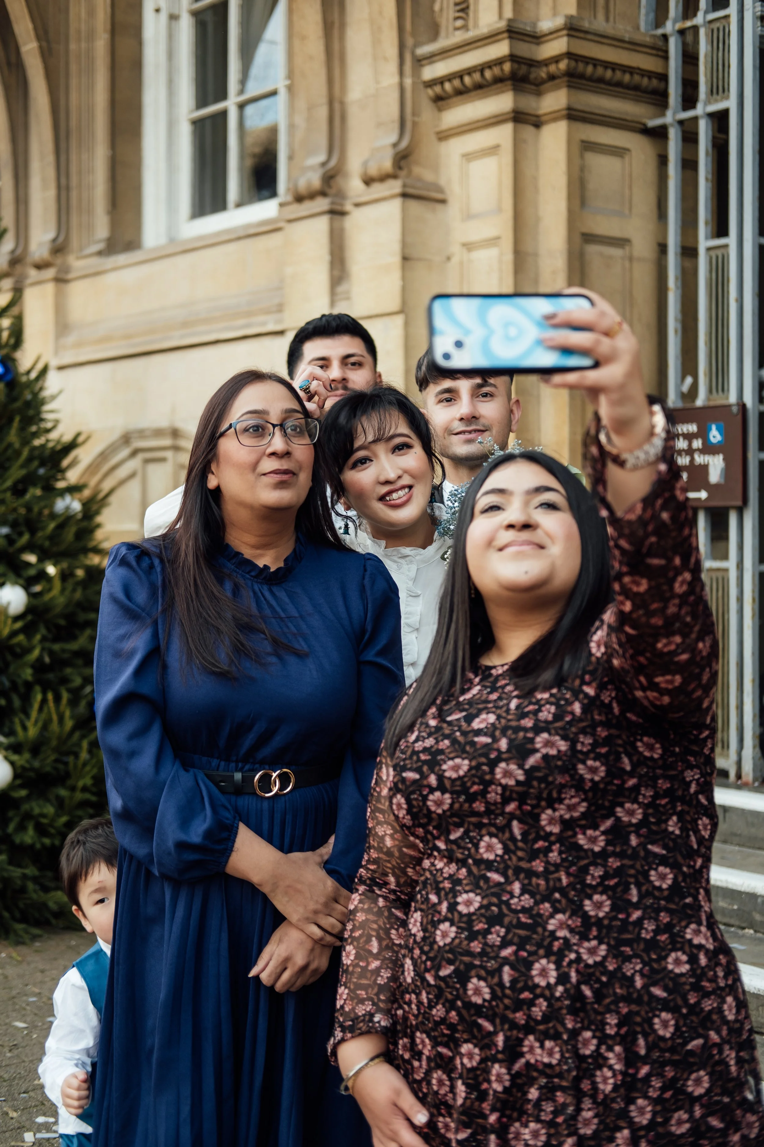 A group of five people taking a selfie outdoors in front of a historic building and Christmas tree.
