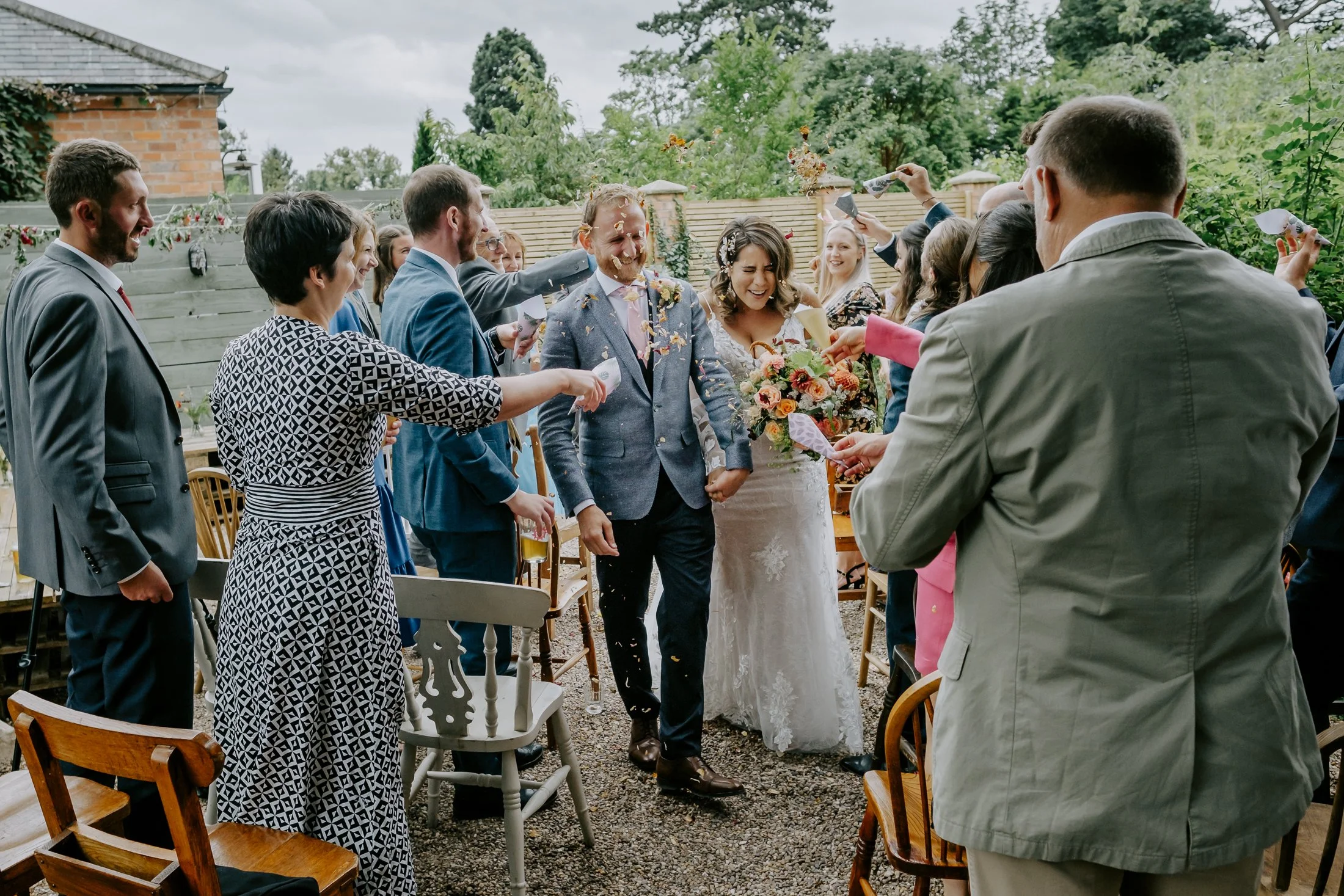 Bride and groom walking through a shower of confetti during their outdoor wedding, surrounded by friends and family.