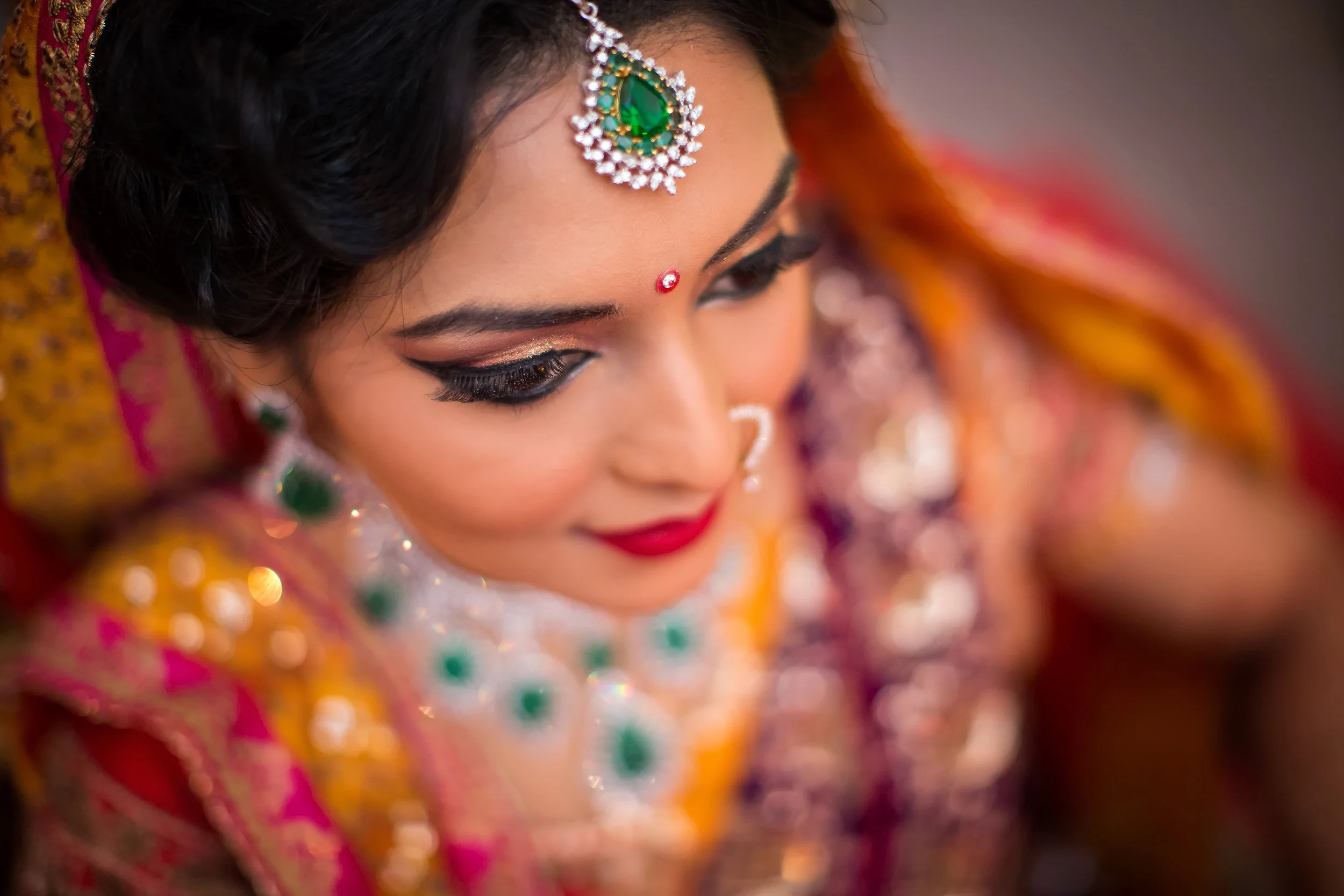 Close-up of an Indian woman dressed in traditional wedding attire with jewelry and bright makeup.