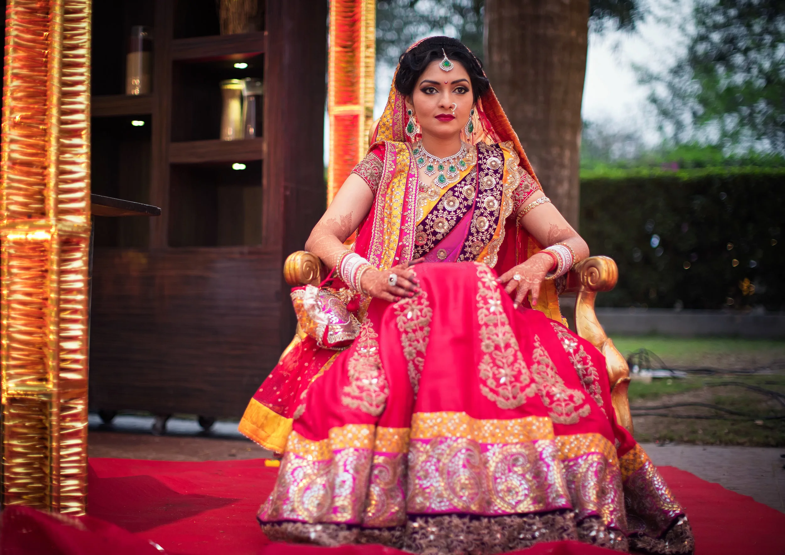 A woman in a traditional Indian bridal outfit sitting on a decorated golden chair outdoors.