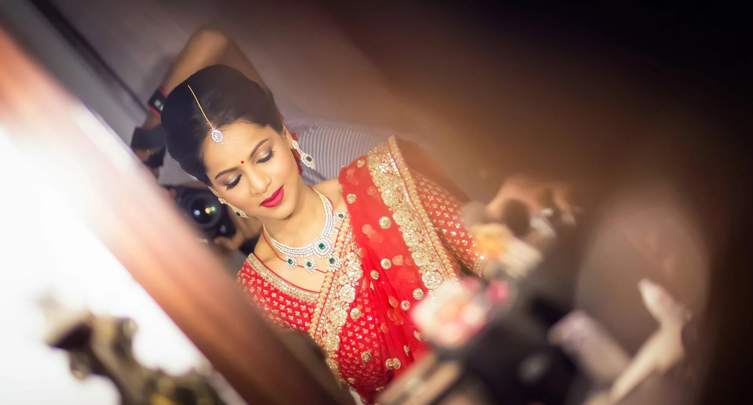 A woman dressed in traditional Indian bridal attire, wearing a red saree with gold embroidery and matching jewelry, with her eyes closed and makeup done.