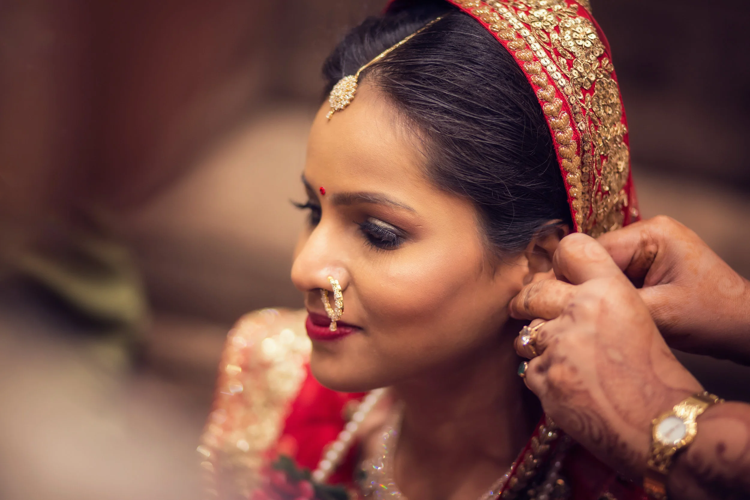 A woman in traditional Indian wedding attire being adorned with jewelry.