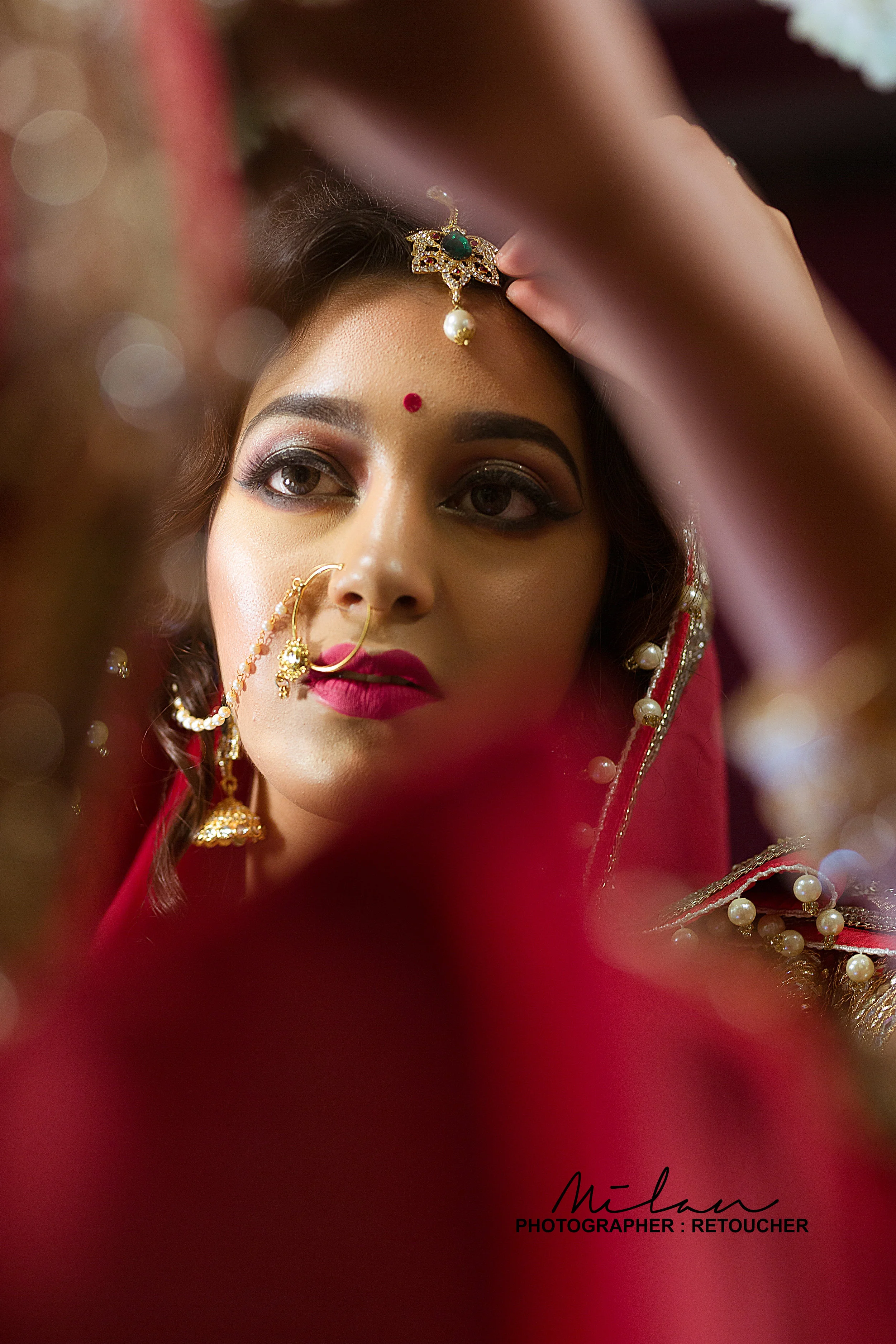 A woman dressed in traditional Indian attire, wearing jewelry including a nose ring, earrings, a bindi on her forehead, and a headpiece, looking into a mirror.