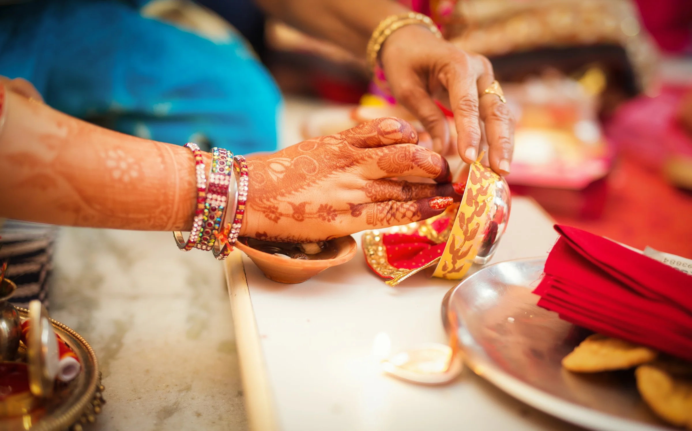 Close-up of hands decorated with colorful bangles and henna applying a red and gold fabric to a small deity idol during a festival or religious ceremony.