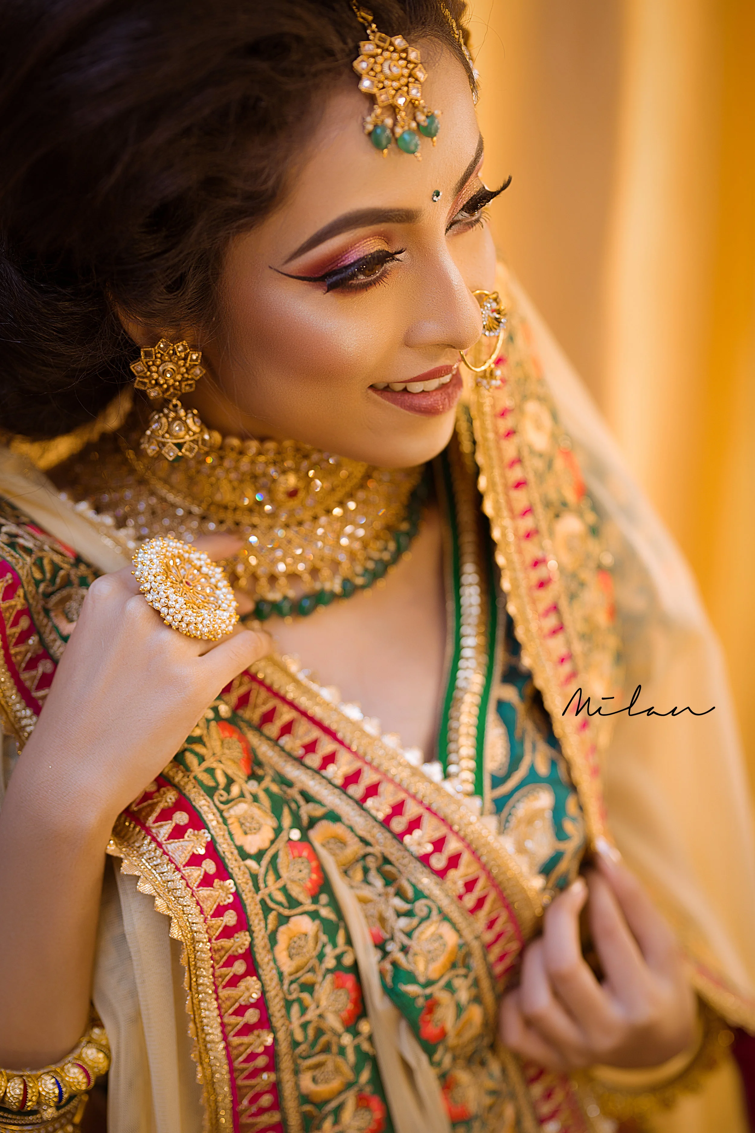 A woman wearing traditional Indian bridal attire with gold jewelry, including earrings, necklace, and ring, smiling softly.