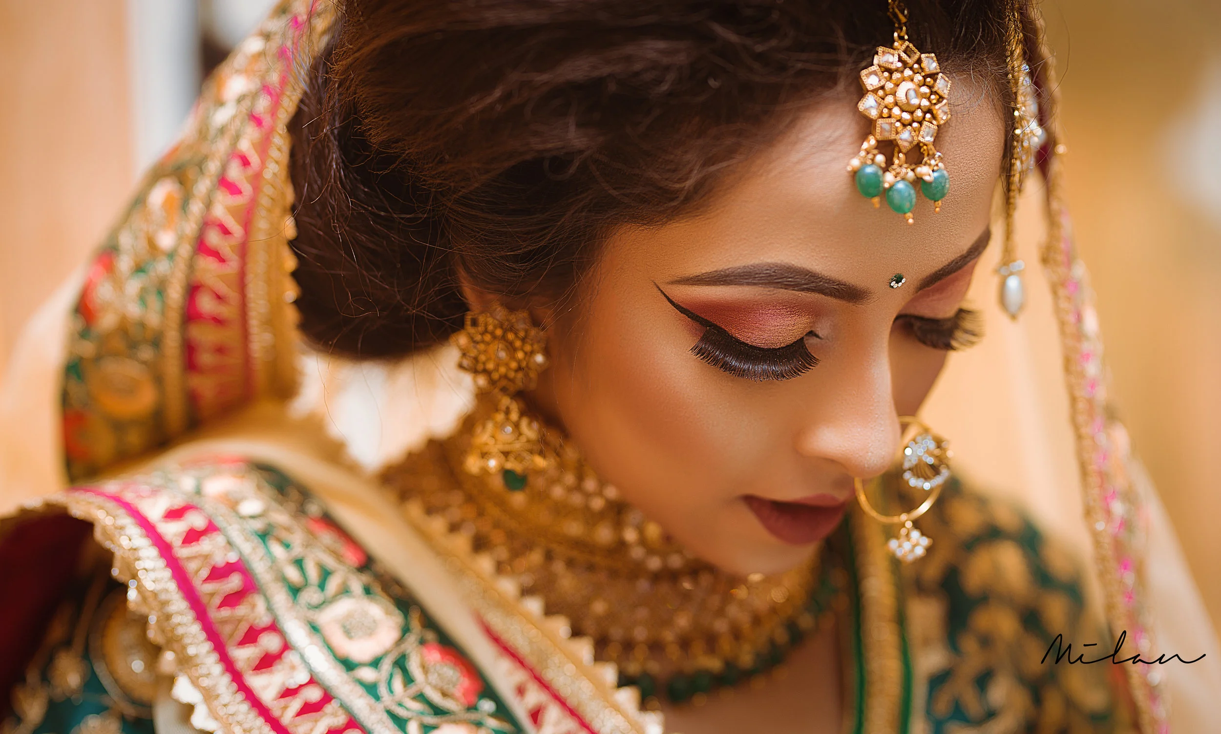 Close-up of a woman dressed in traditional Indian bridal attire, wearing gold jewelry and makeup with pink and gold eye shadow, decorated with a green and gold dupatta.