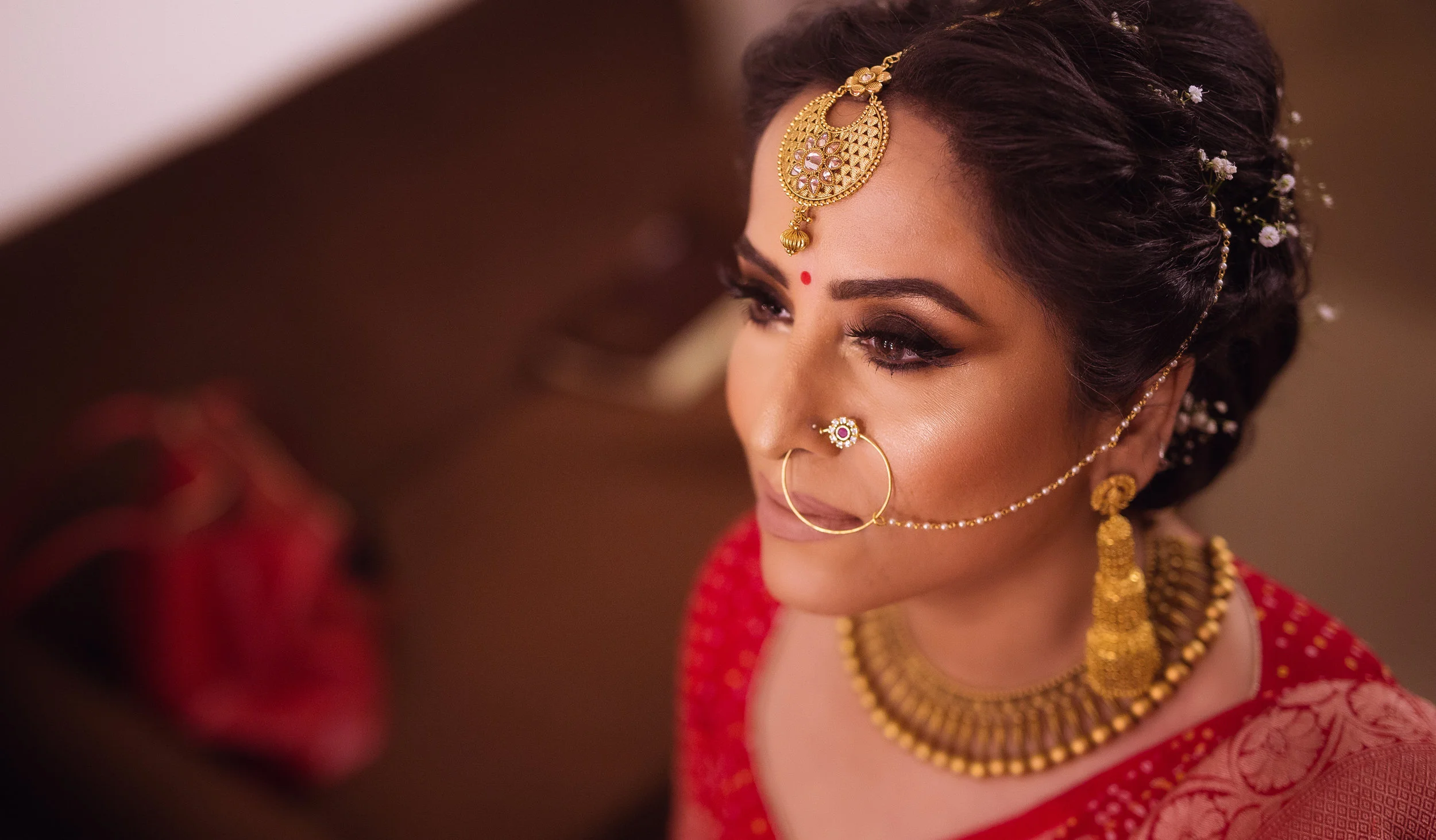 A woman dressed in traditional Indian bridal attire with jewelry, makeup, and flowers in her hair.