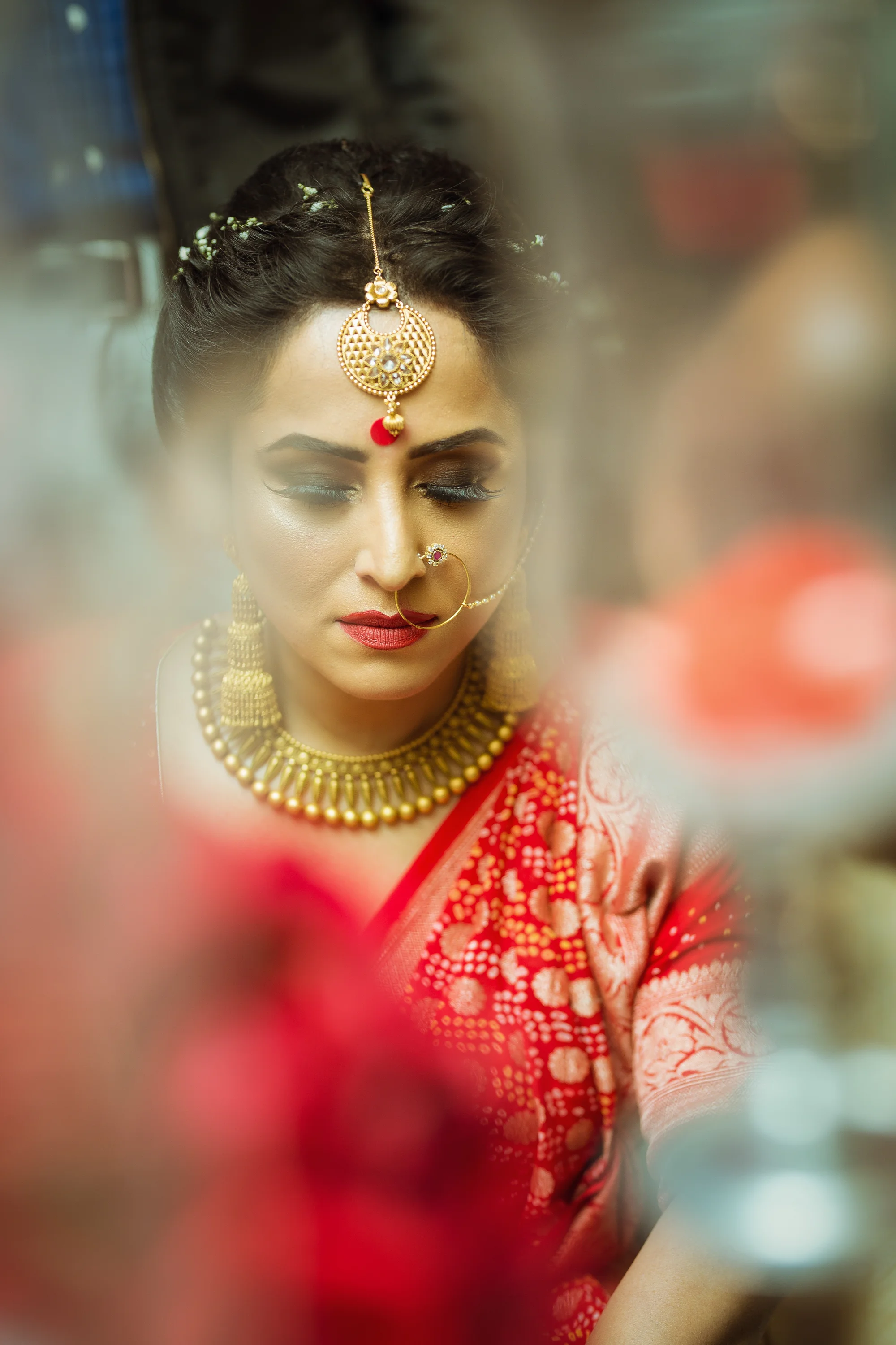 A woman dressed in traditional Indian attire with gold jewelry and makeup, looking down with her eyes closed.