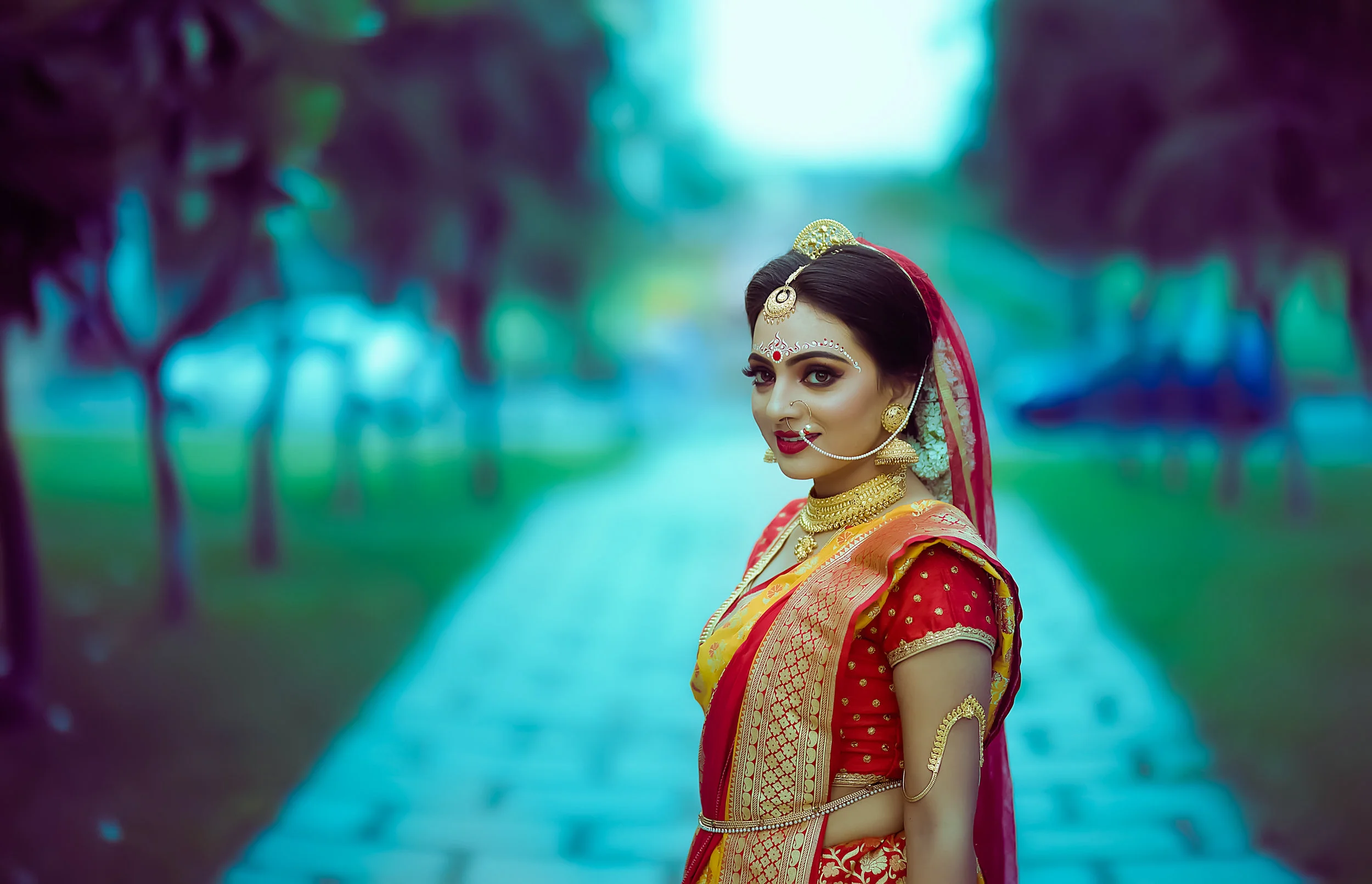 A woman in traditional Indian attire with jewelry standing on a pathway in a park.