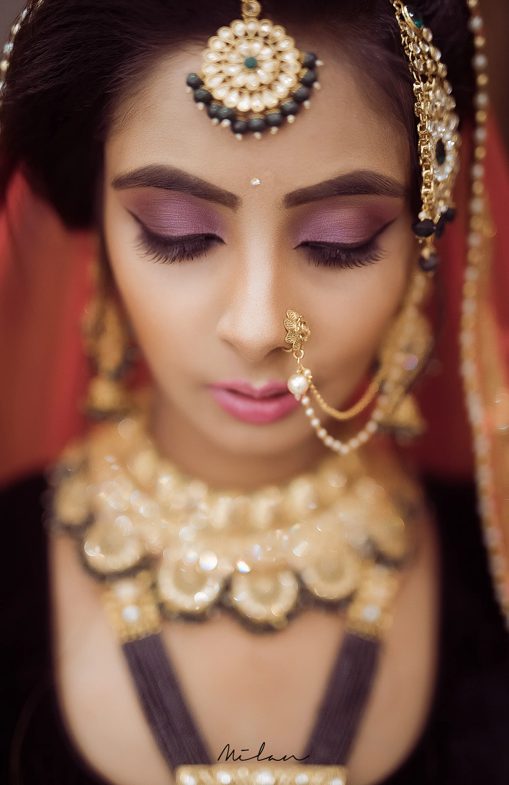 Close-up of a woman with traditional Indian jewelry and makeup, with her eyes closed.