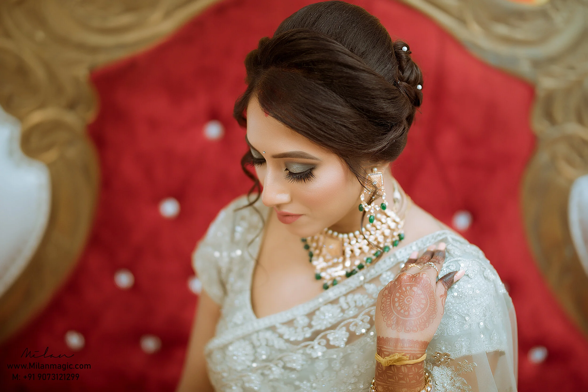 A woman dressed in traditional bridal attire sitting on a red and gold ornate throne, showing her henna-decorated hand.