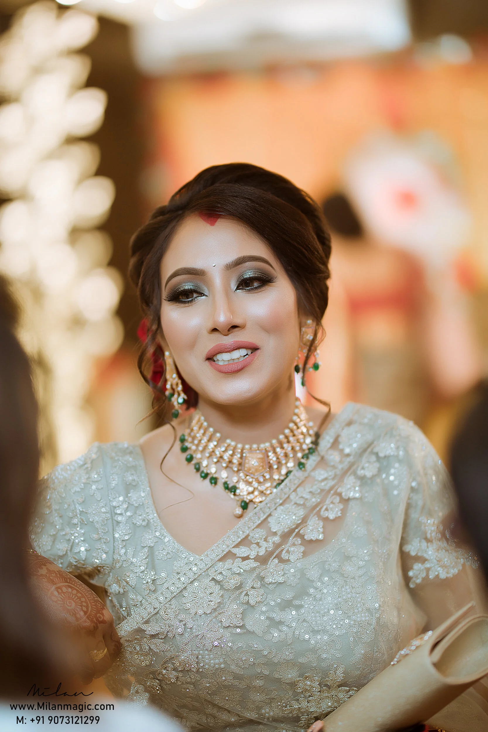 A woman dressed in traditional Indian attire with elaborate jewelry, including a necklace, earrings, and a headpiece, smiling during a celebration or wedding.