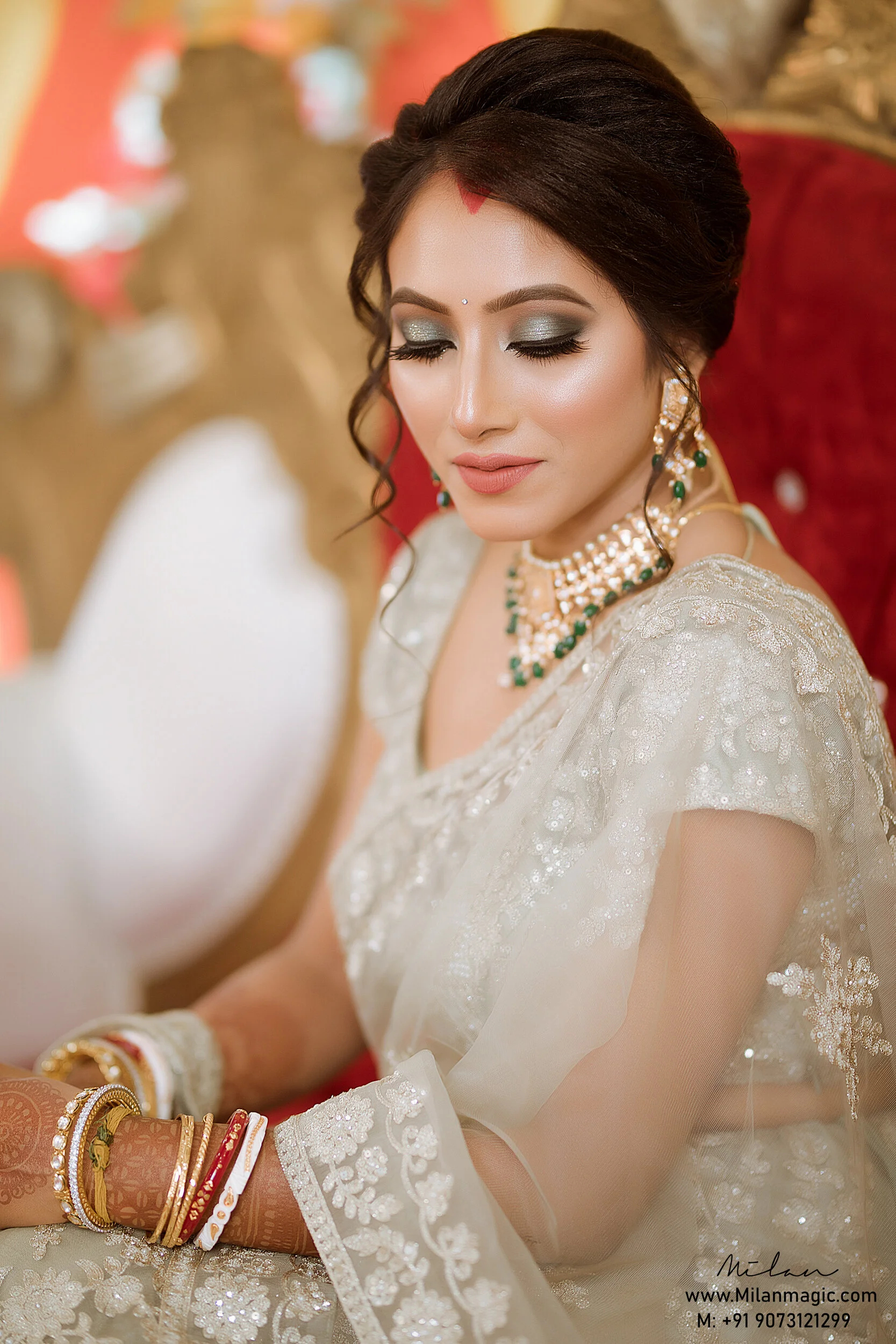 Close-up of a bride wearing traditional Indian wedding attire with jewelry, makeup, and henna designs on her hands, sitting on an ornate chair.