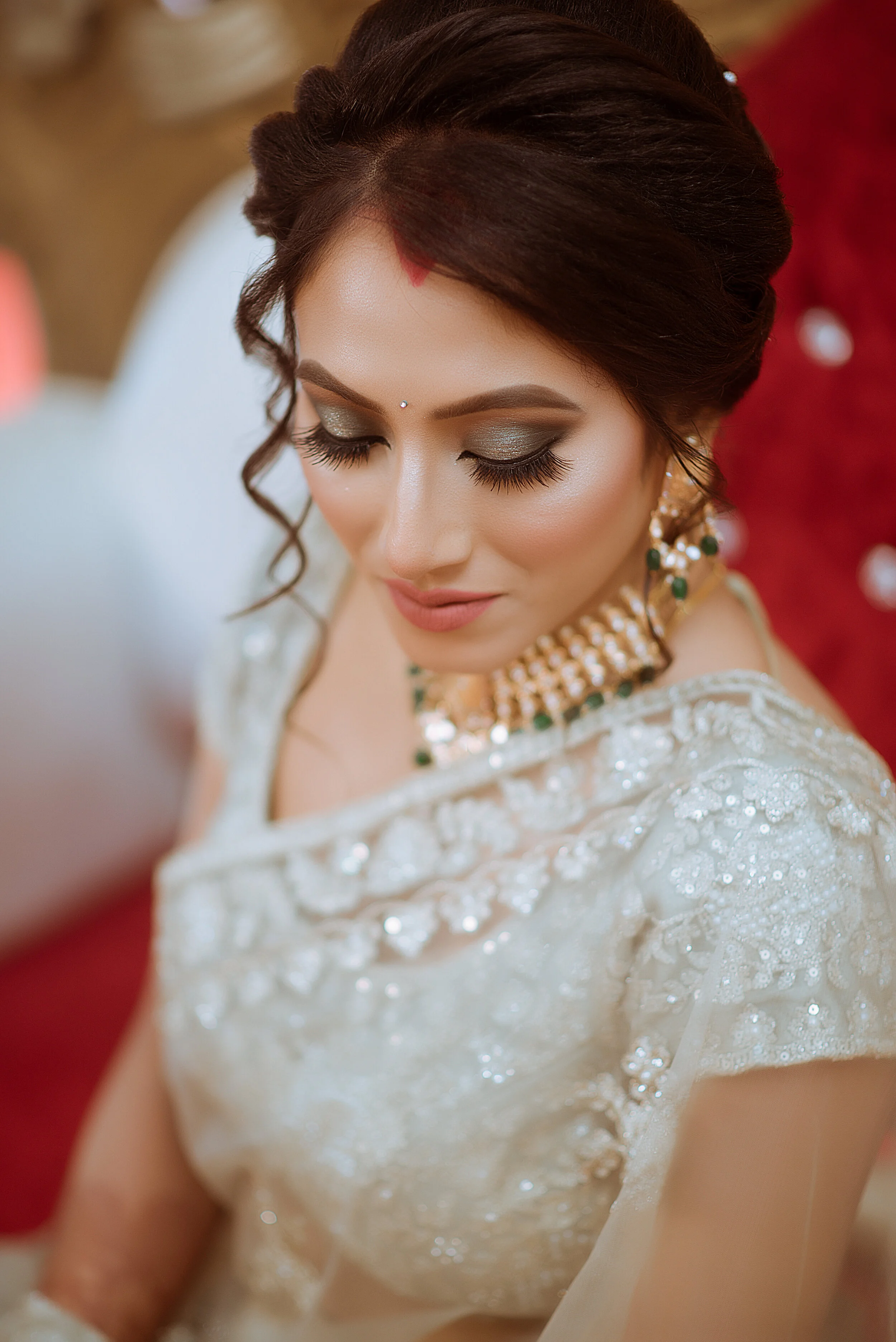 Close-up of a bride with makeup, jewelry, traditional attire, and a bindi, looking downward during her wedding ceremony.