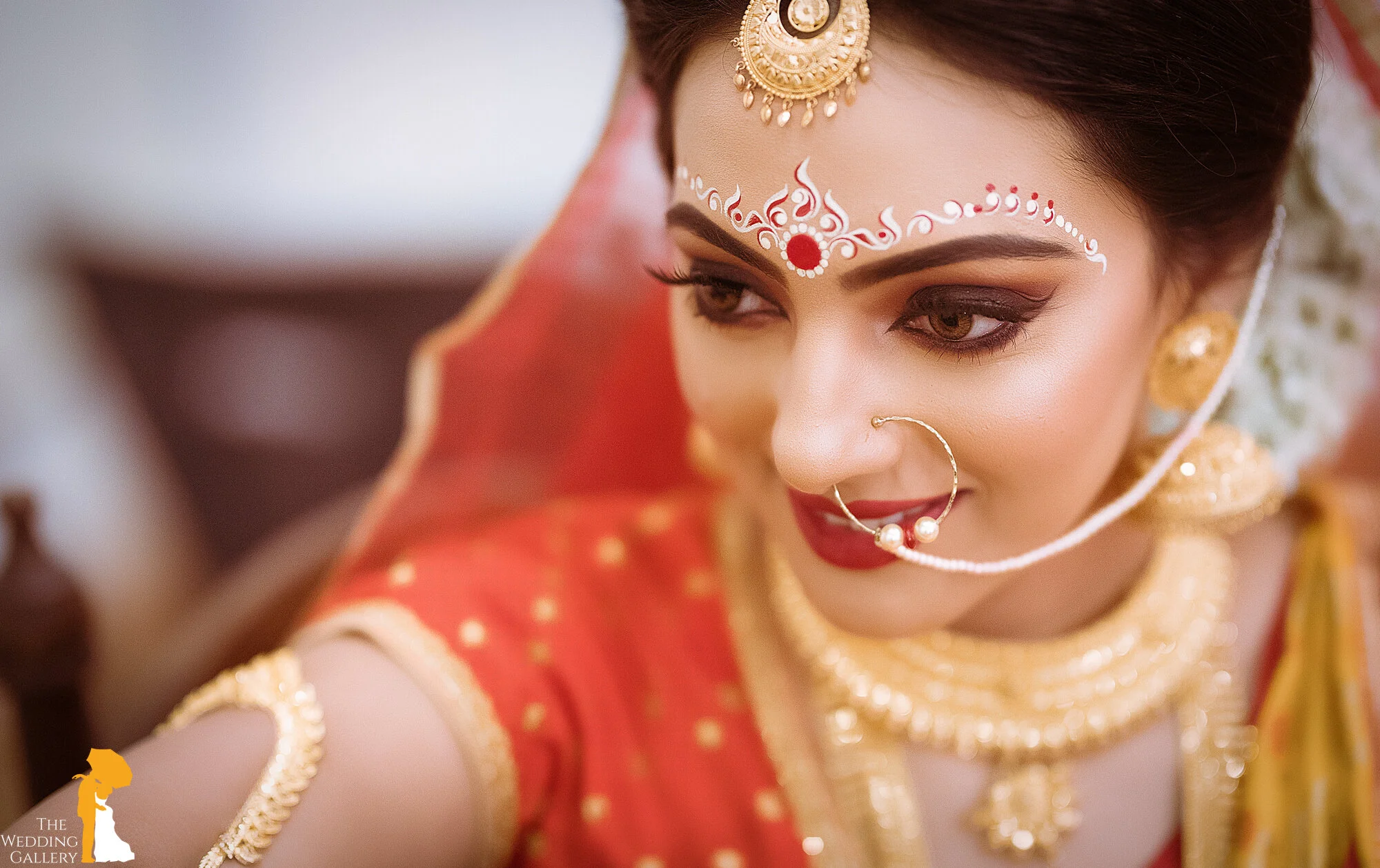 Close-up of a woman dressed in traditional Indian bridal attire with intricate jewelry and makeup, looking to the side.