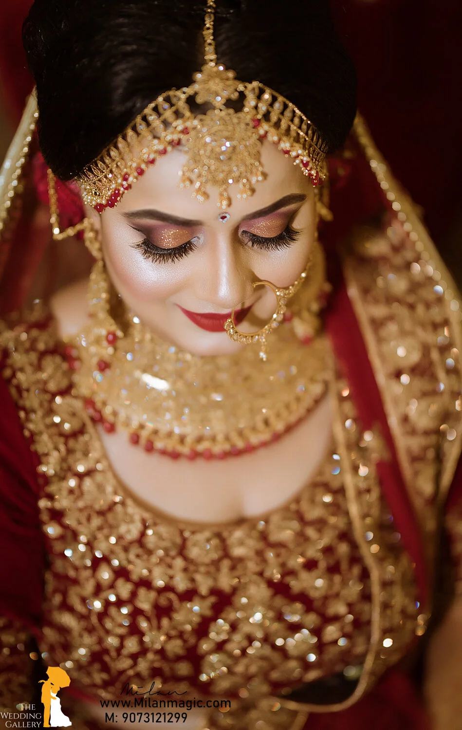 A bride dressed in traditional Indian wedding attire with elaborate gold jewelry and makeup, looking downward with her eyes closed.