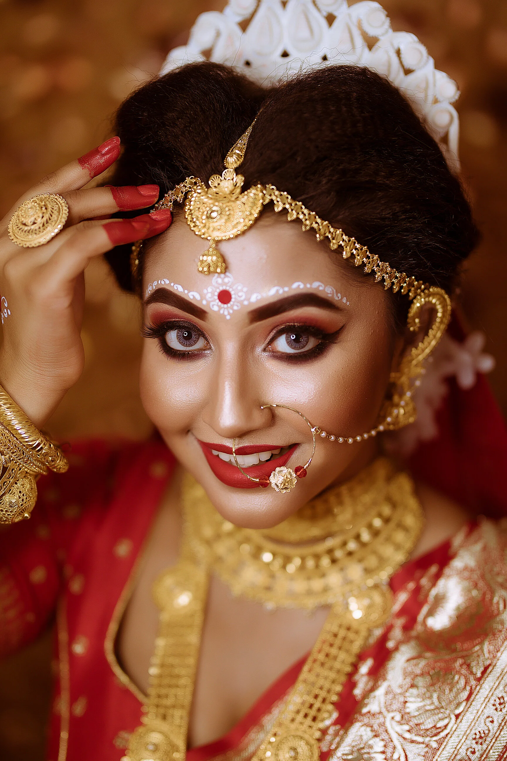 A woman dressed in traditional Indian bridal attire with intricate gold jewelry, bold makeup, and traditional adornments, smiling at the camera.