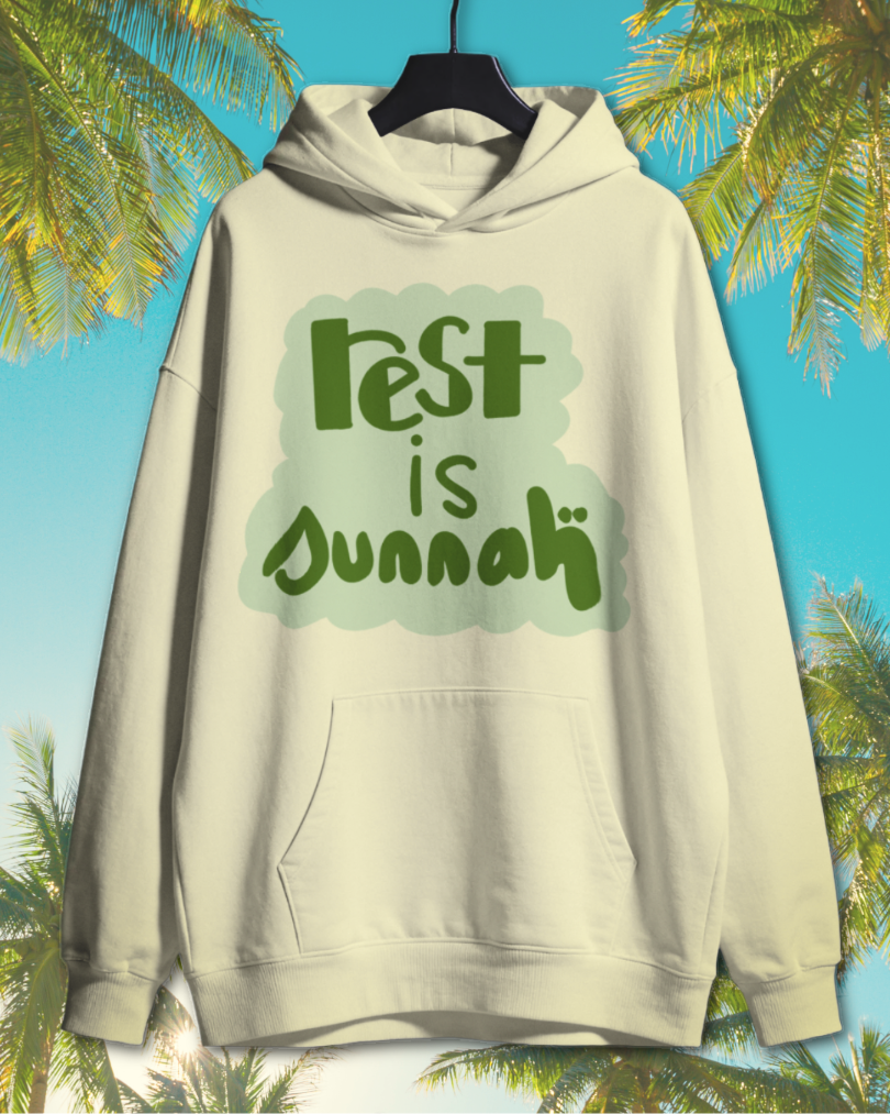 White hoodie with green text saying 'rest is funnuh' hanging against a background of palm trees and a blue sky.