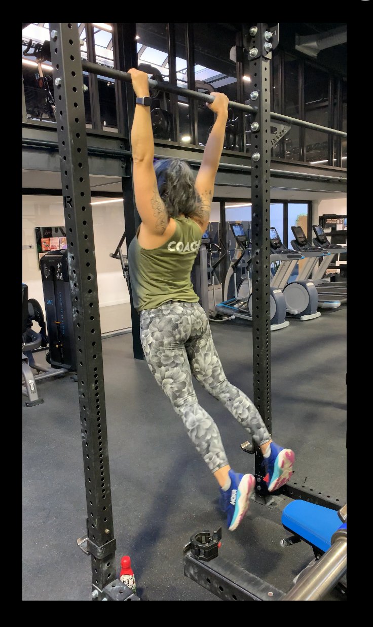 Woman strength training hanging from pull-up bar demonstrating upper body strength