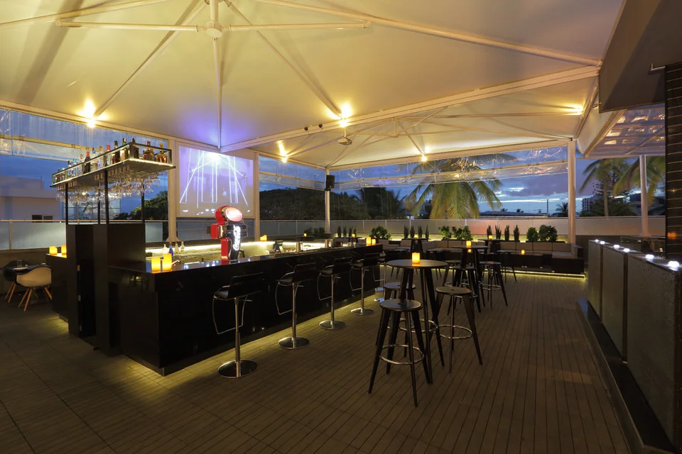 Troika is a spacious bar with a great view, exactly the kind of uncrowded place to hang out in peace. It has a variety of seating arrangements centered around an island bar and is open on all sides, making it a picturesque sight in the evenings. Wooden decking floor, 3 D tiles for wall cladding, all imported lounge furniture and tensile structure for outdoor protection, make it a premium rooftop experience in cool and breezy Bangalore.