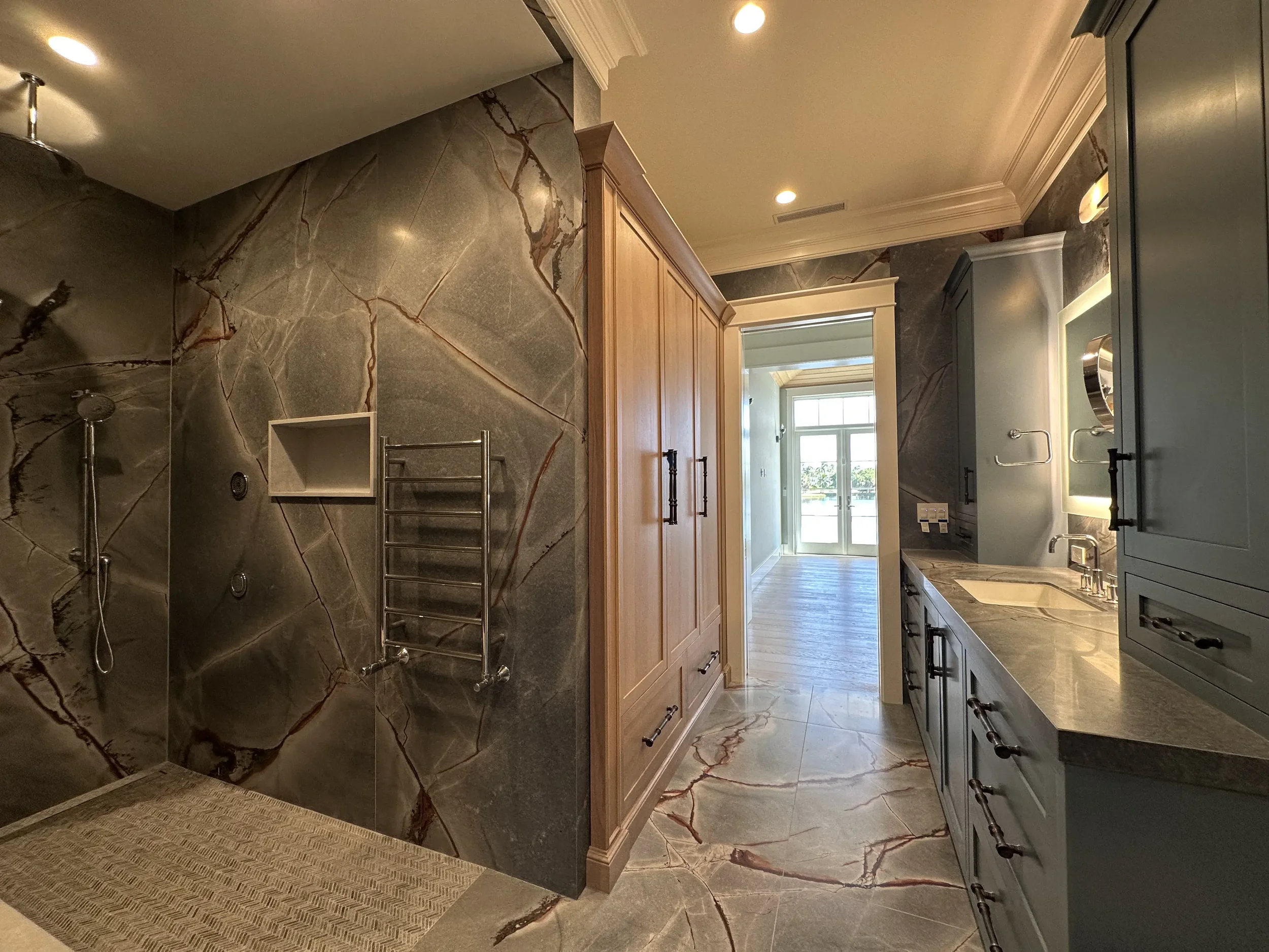 Luxury bathroom with stone slab walls, walk-in shower, long vanity, wood storage cabinet, wall sconces, and marble-look flooring.