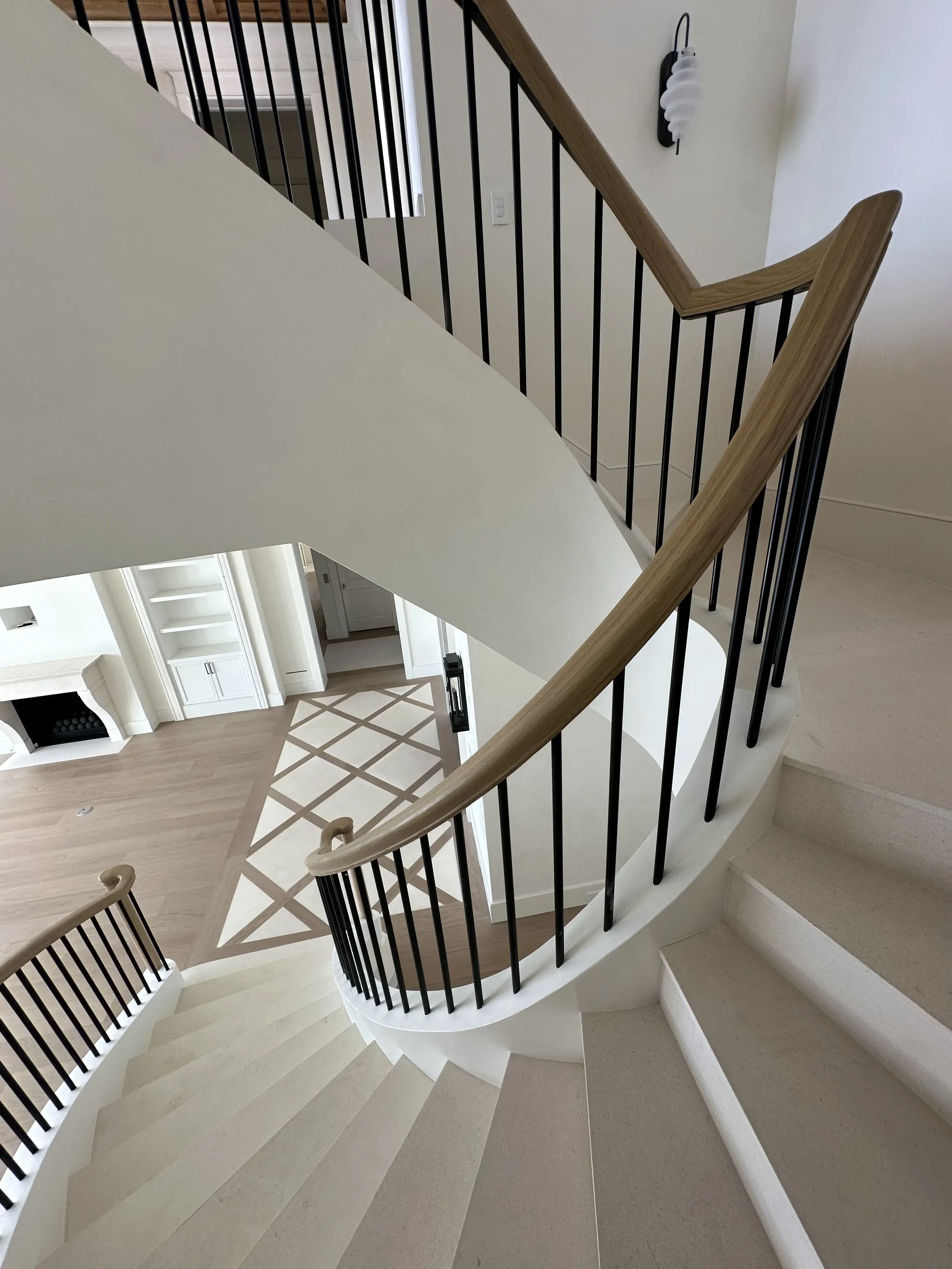 Curved interior staircase with light stone treads, black metal balusters, wood handrail, and view down to the foyer.