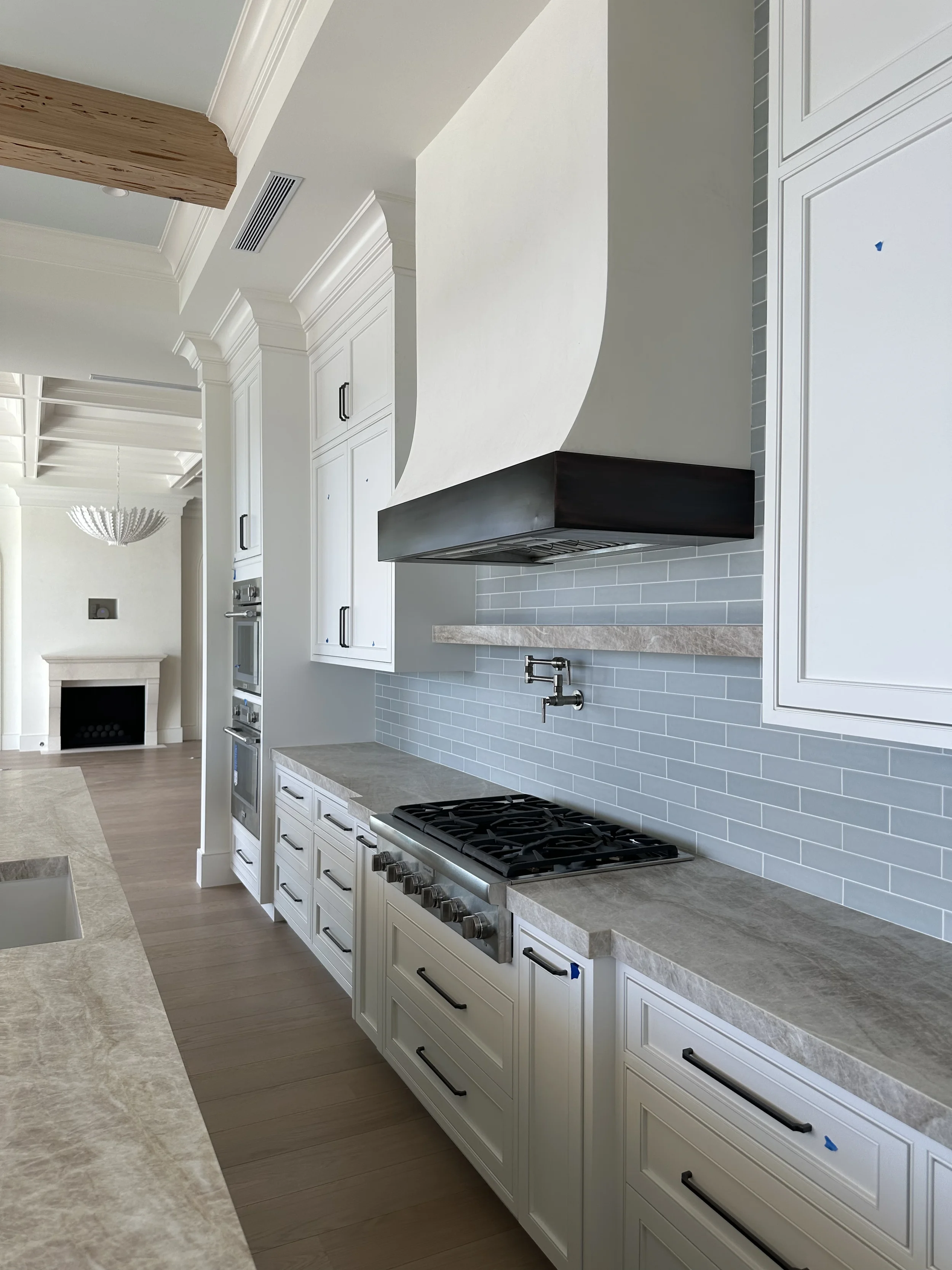 White kitchen with gas range, custom range hood, gray subway tile backsplash, stone countertops, and built-in cabinetry.