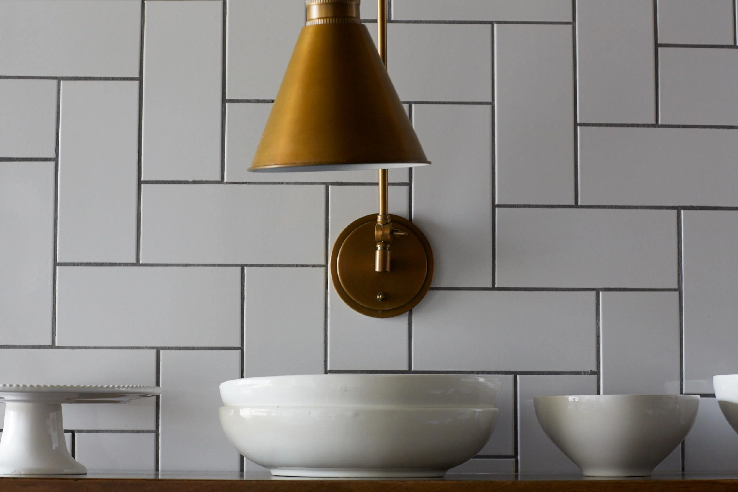 Porcelain Dishes & Brass Sconce Against A White Tile Wall