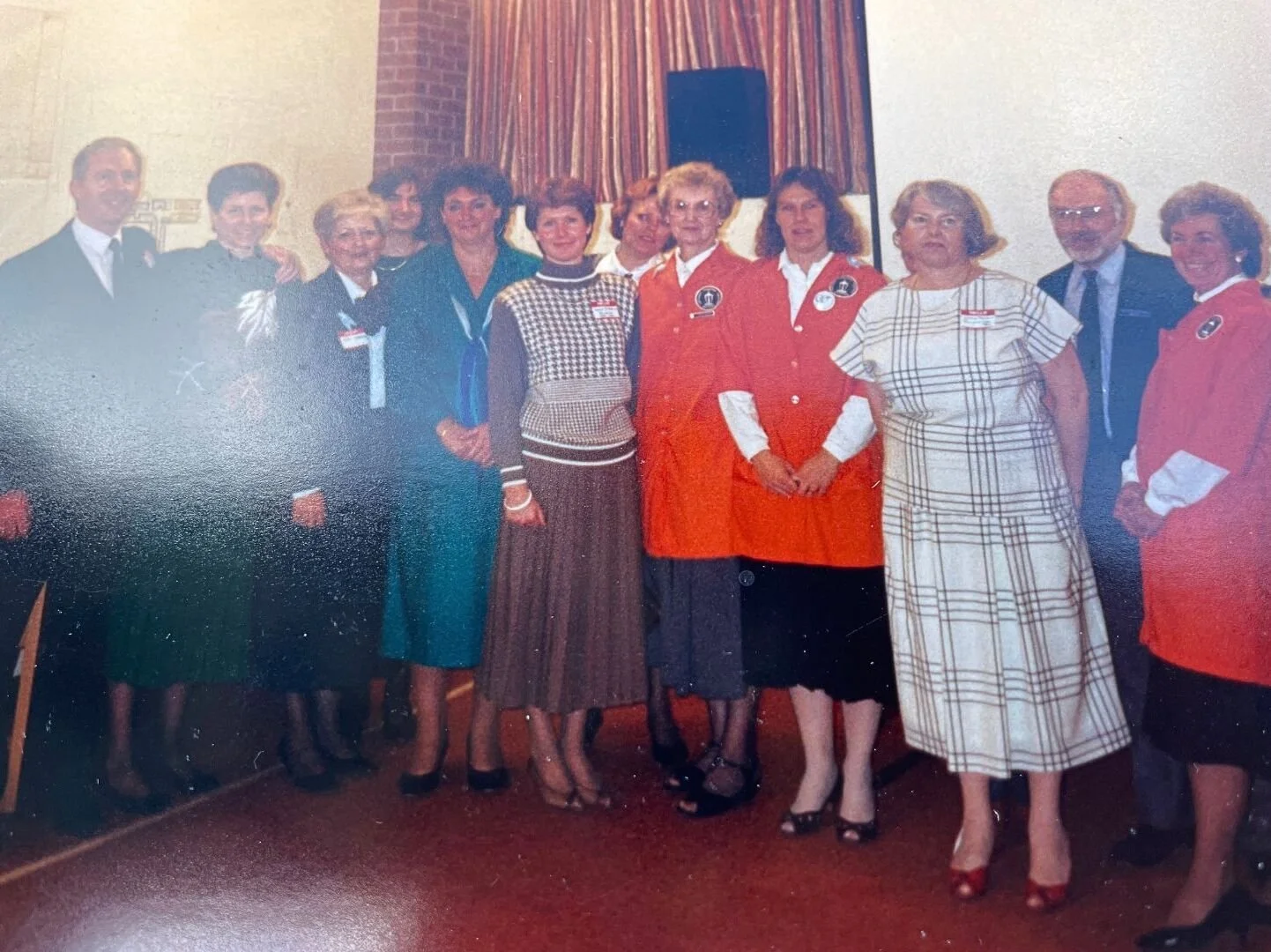 The early Palliative Care team stands together indoors at a hospital event. The group includes team members, community supporters, and volunteers wearing orange jackets.