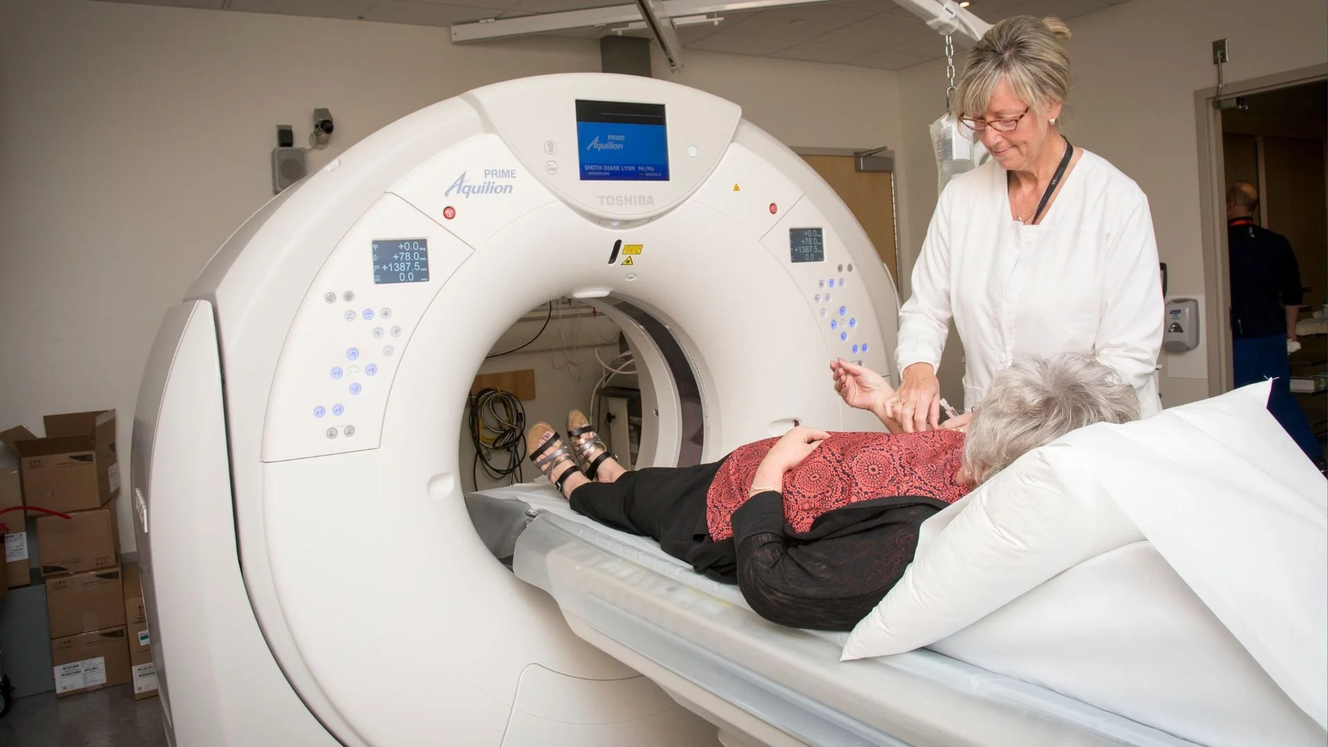 Healthcare professional helping an elderly patient enter an MRI machine in a hospital imaging room.