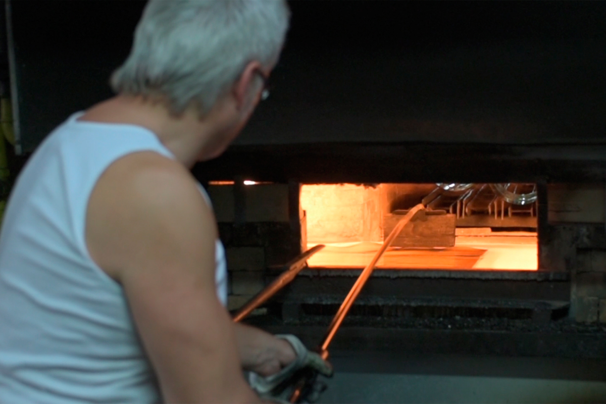 Glass is re-heated and the sides fall flat. A worker "irons" out any bumps.