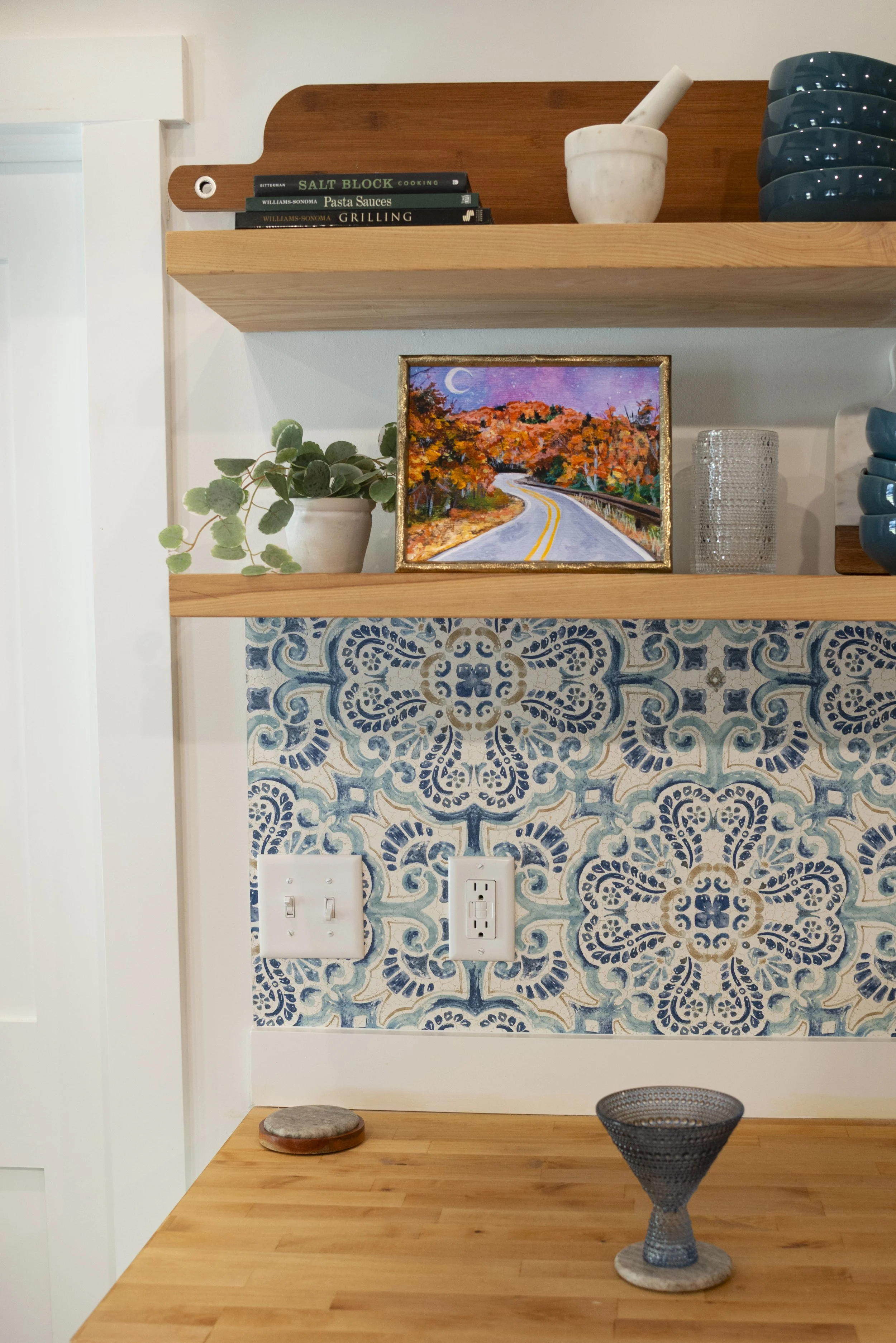 Autumn Blue Ridge Parkway print in a frame, placed on a kitchen shelf in a modern kitchen with wood tones and colorful, blue decor.