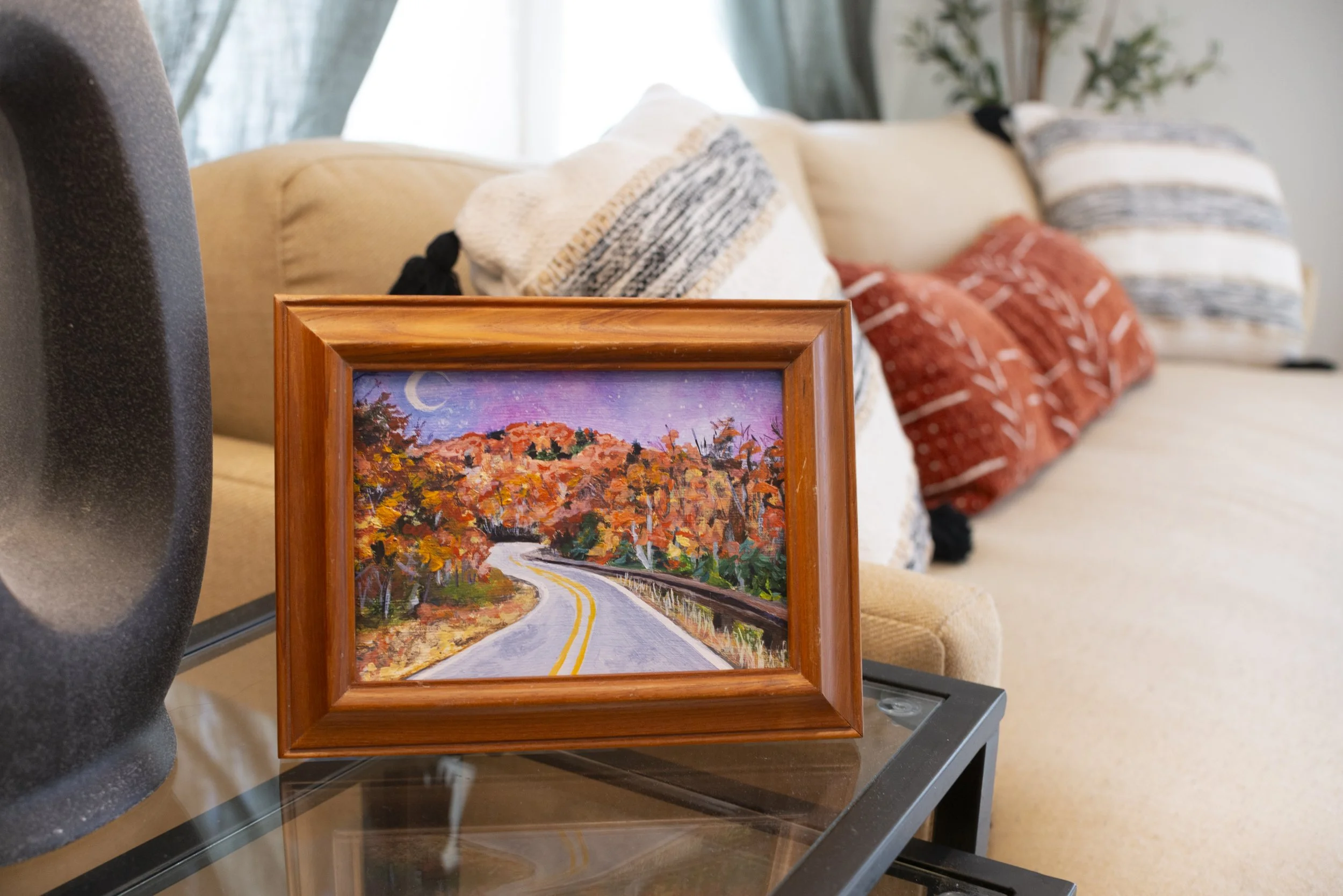 A framed print of a Blue Ridge Parkway overlook in the fall, displayed on a side table in front of a cozy couch with bohemian patterned throw pillows.