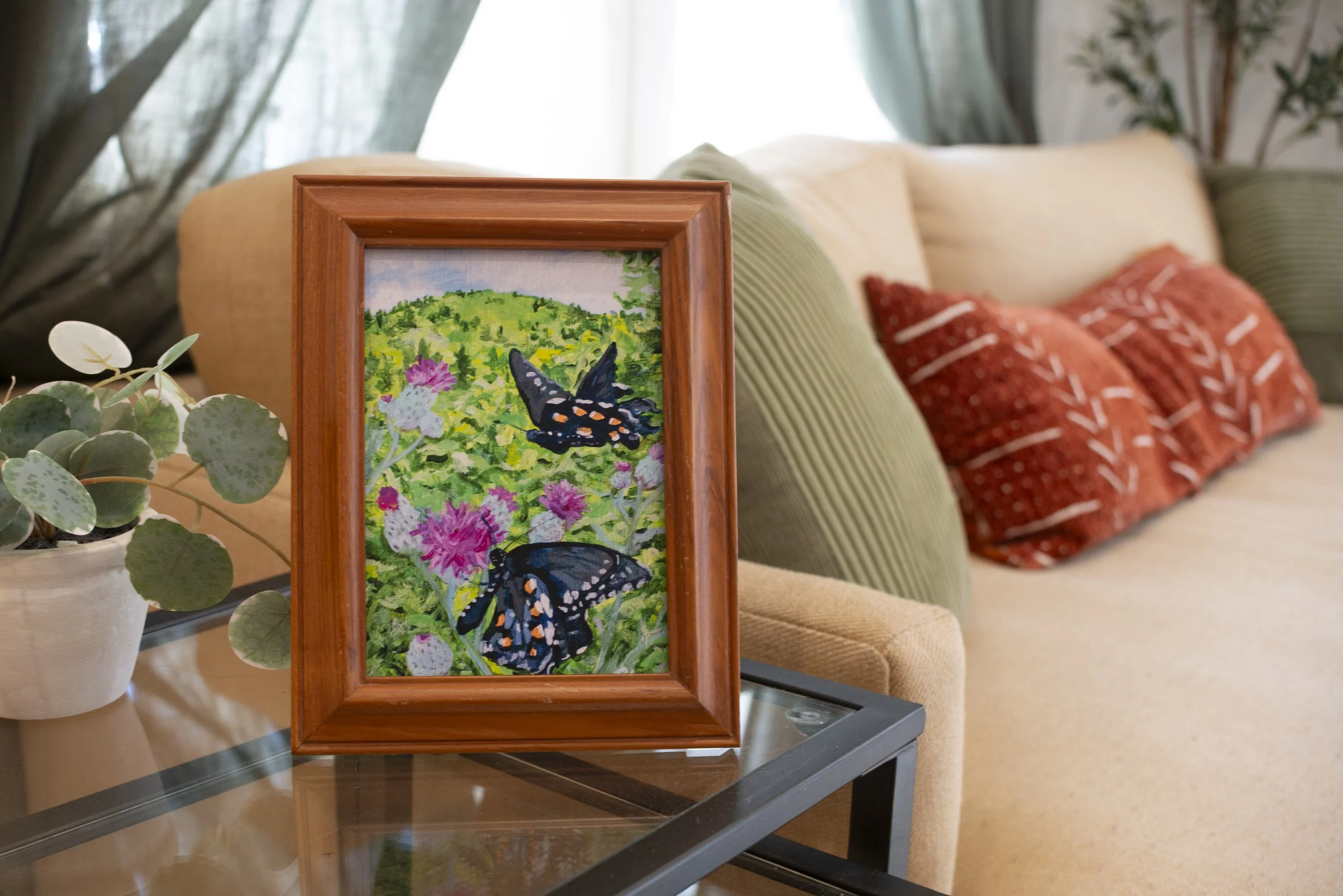 A framed Swallowtail butterflies art print on a side table in front of a couch with bohemian patterned pillows.
