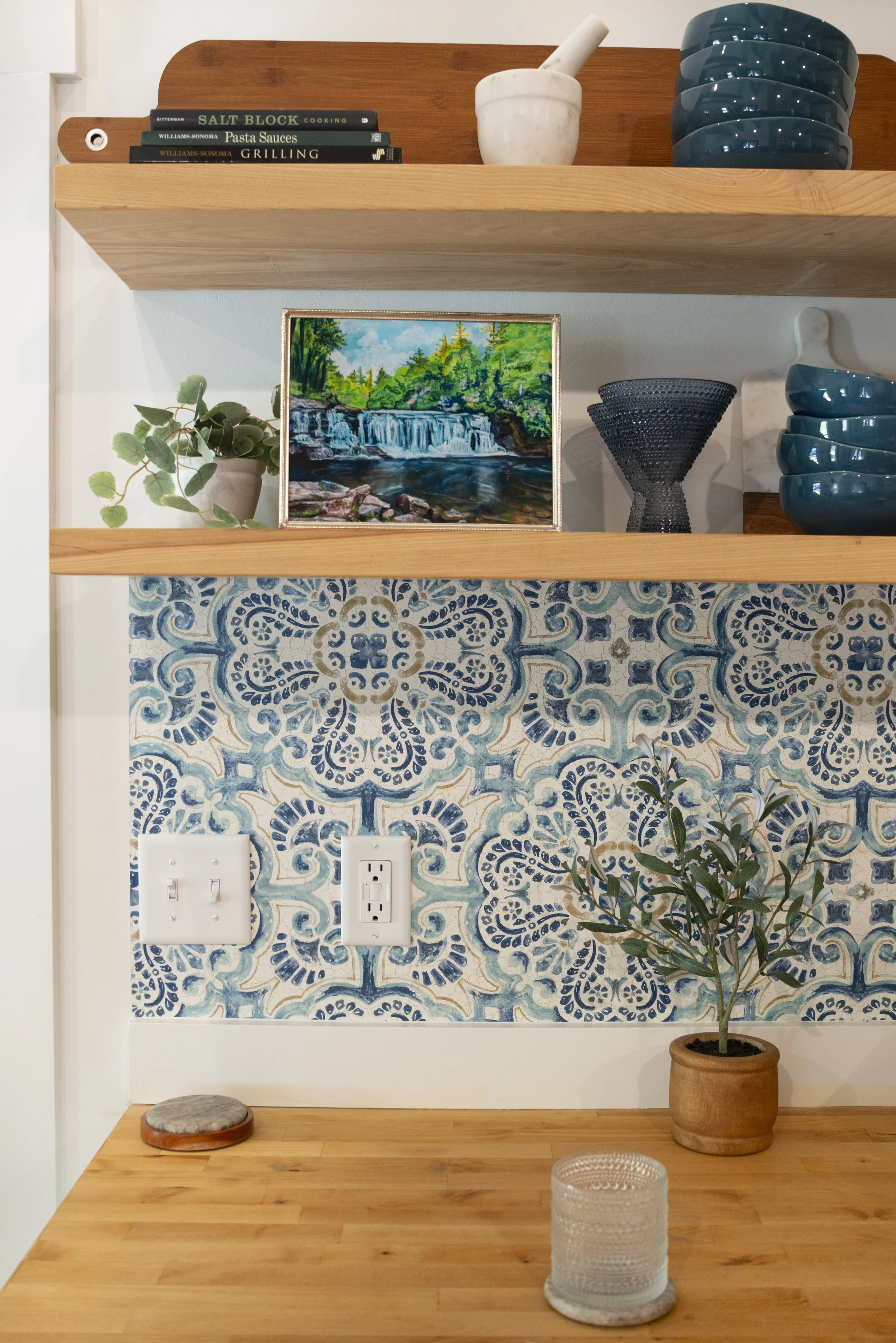 A framed print of Hooker waterfall in DuPont Forest, displayed on a kitchen shelf in a cozy, modern kitchen with wooden shelves and colorful accents.