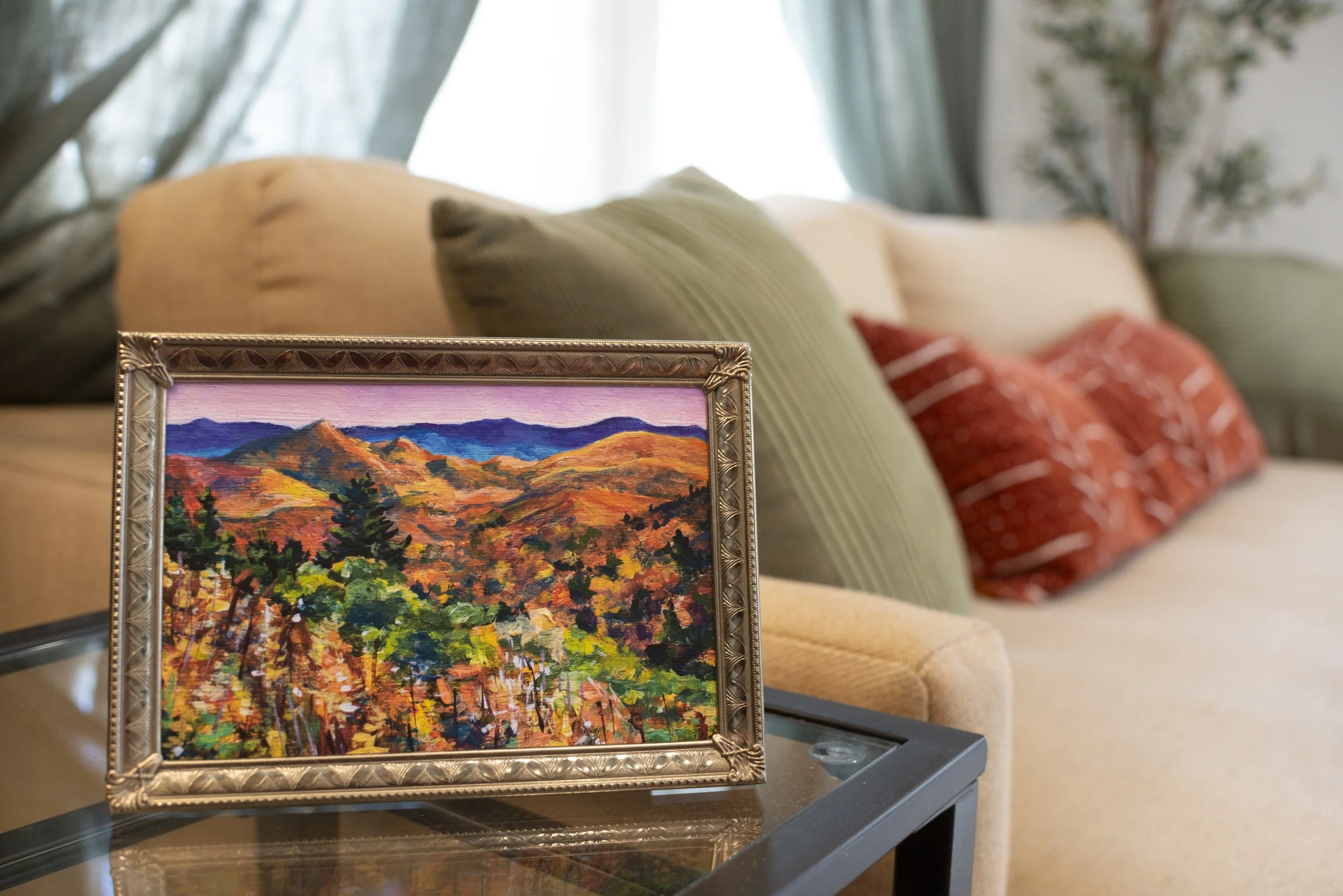 A framed print of a Blue Ridge Parkway overlook in the fall, displayed on a side table in front of a cozy couch with colorful throw pillows.