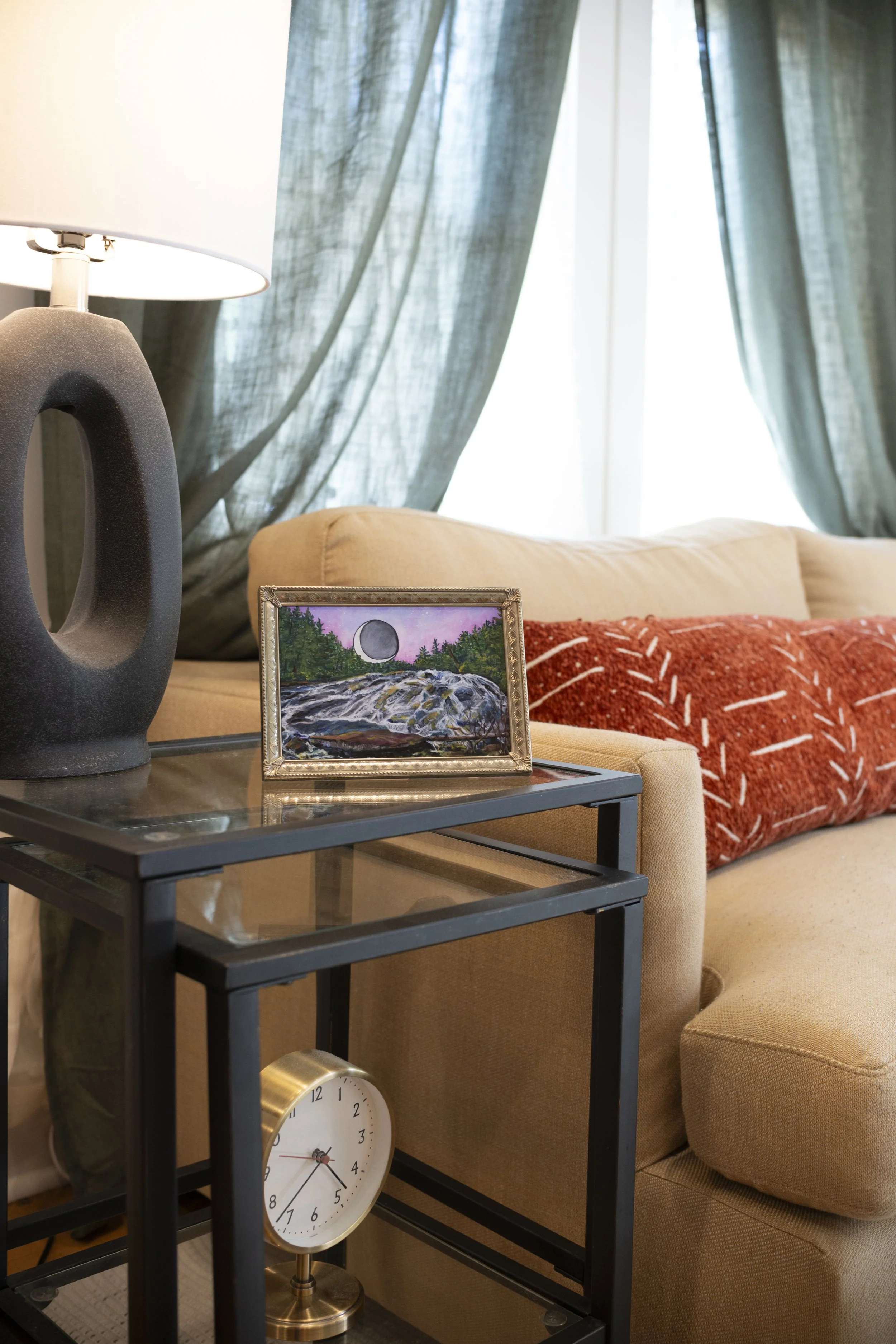 Framed print of Bridal Veil Falls in DuPont Forest, set on a table in a cozy living room with a lamp, gold clock, and warm decorative accents.