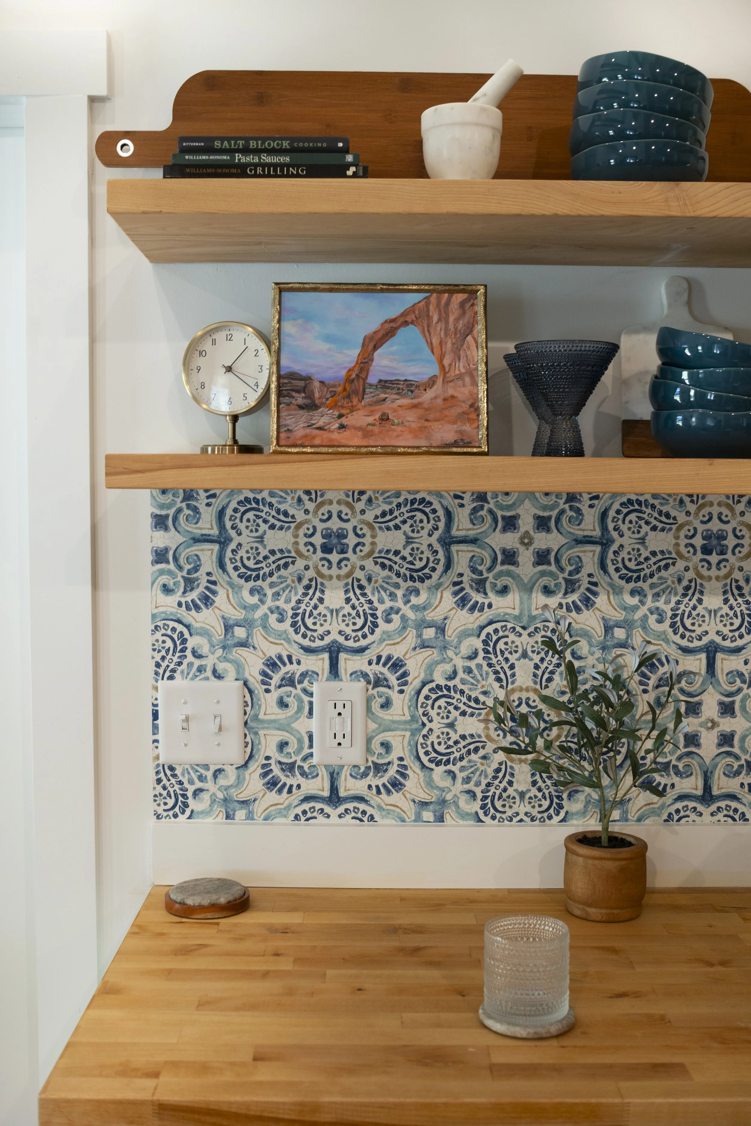 A print of Corona Arch in Moab, UT in a gold frame displayed on a wooden shelf in a cozy, modern kitchen with colorful blue accents.
