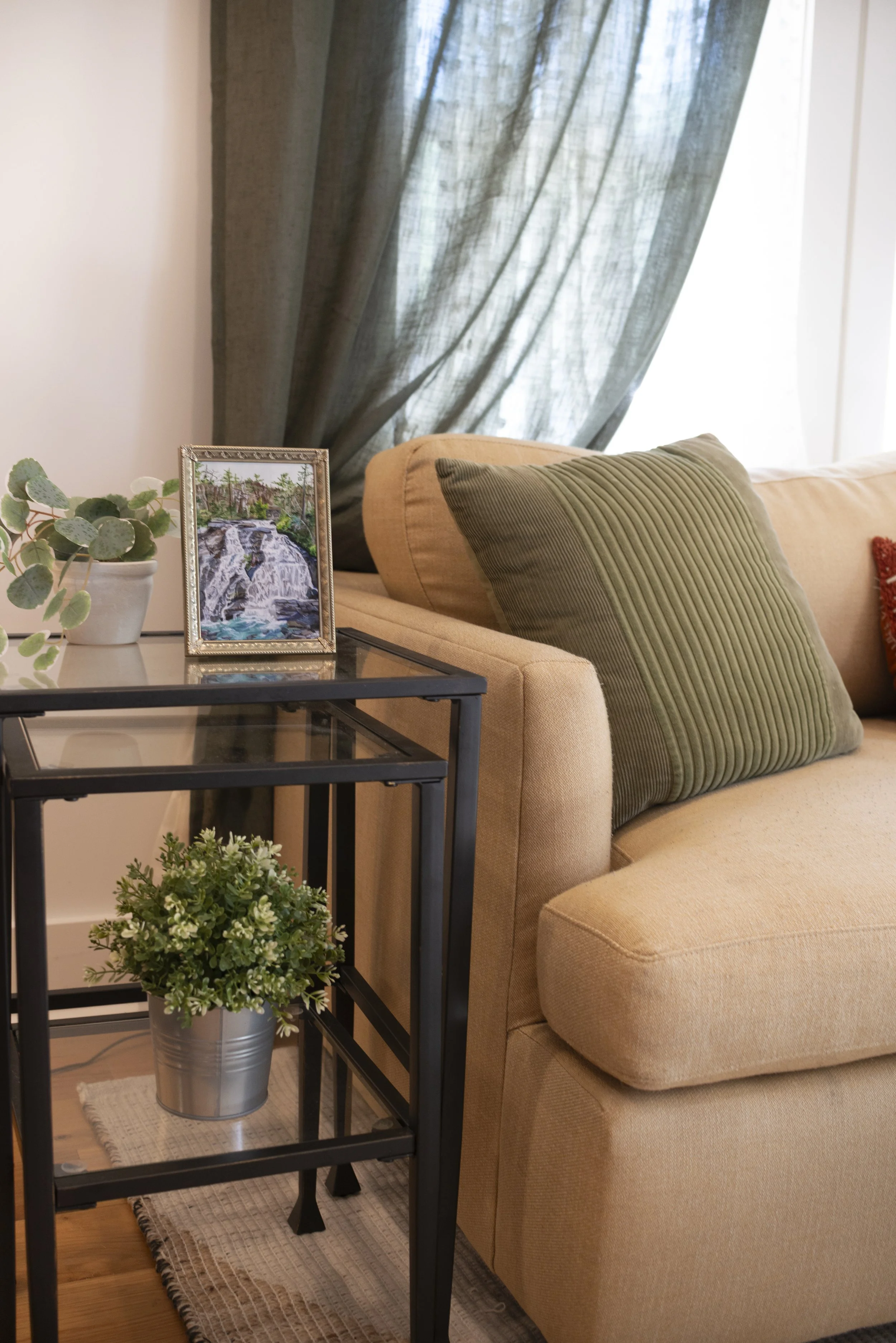 A gold framed art print of a DuPont waterfall, displayed on a side table in a living room next to a cozy couch and indoor plants.