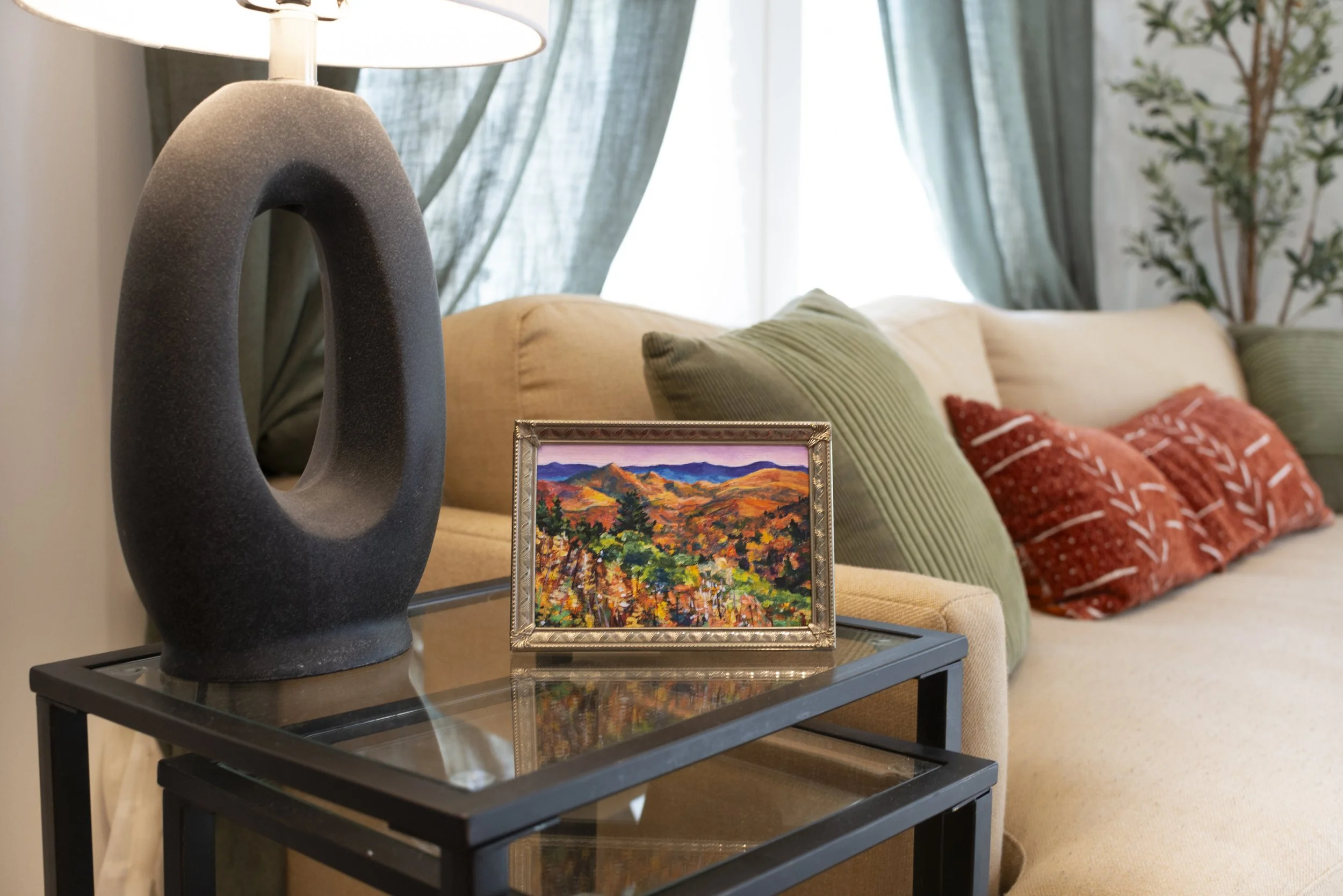 A framed print of a Blue Ridge Parkway overlook in the fall, displayed on a side table in a modern living room next to a couch.
