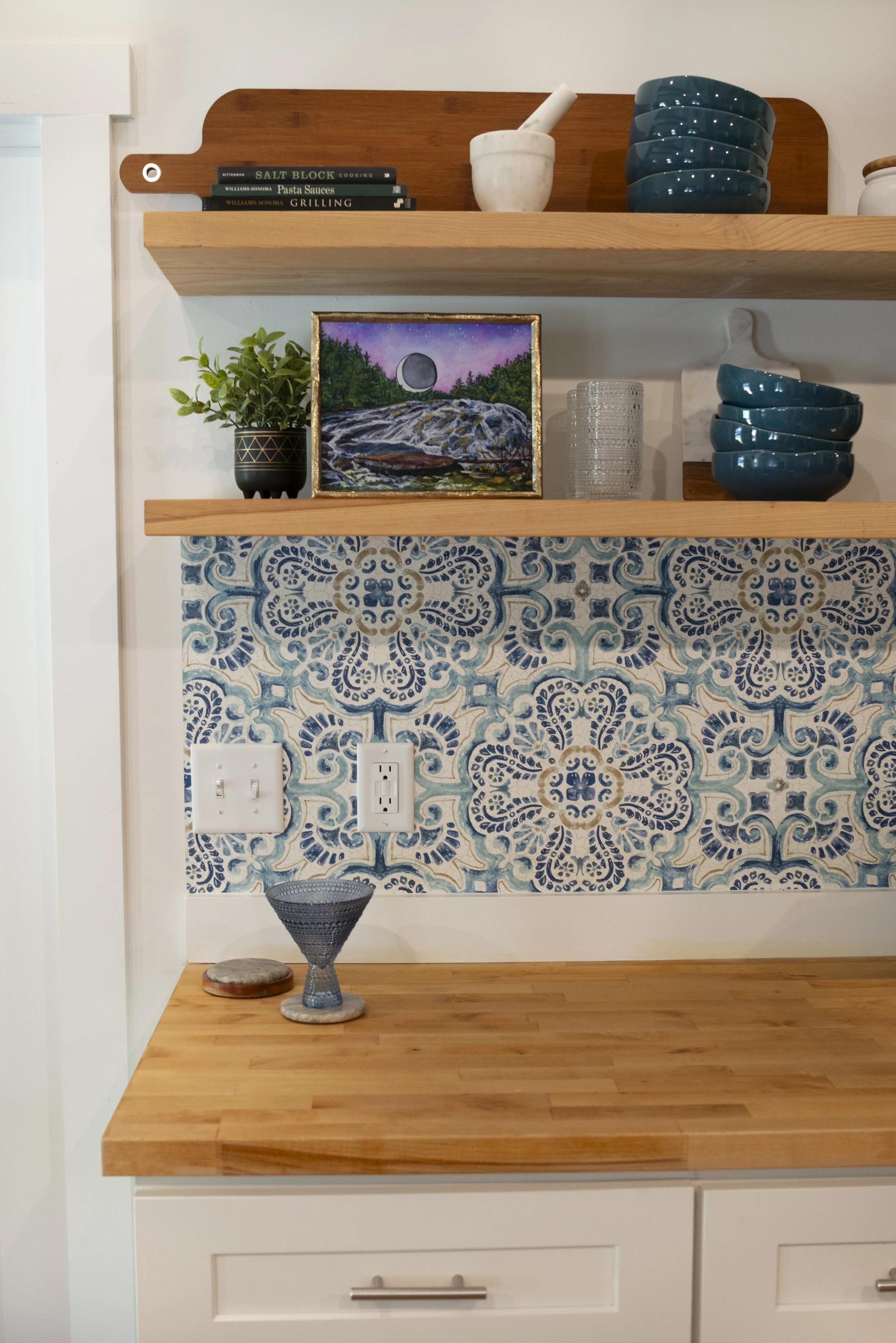 A framed print of Bridal Veil Falls in DuPont Forest, displayed on a kitchen shelf in a cozy, modern kitchen with wooden shelves and colorful accents.