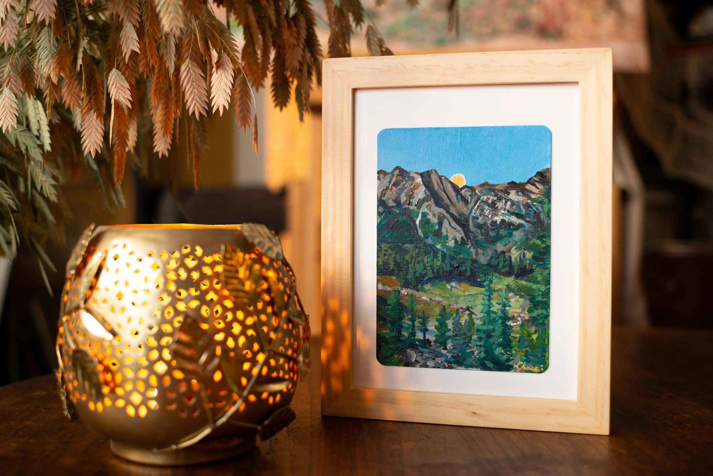 The original artwork framed on a table and styled with a decorative candle holder and dried sea oats hanging over the edge of the frame.