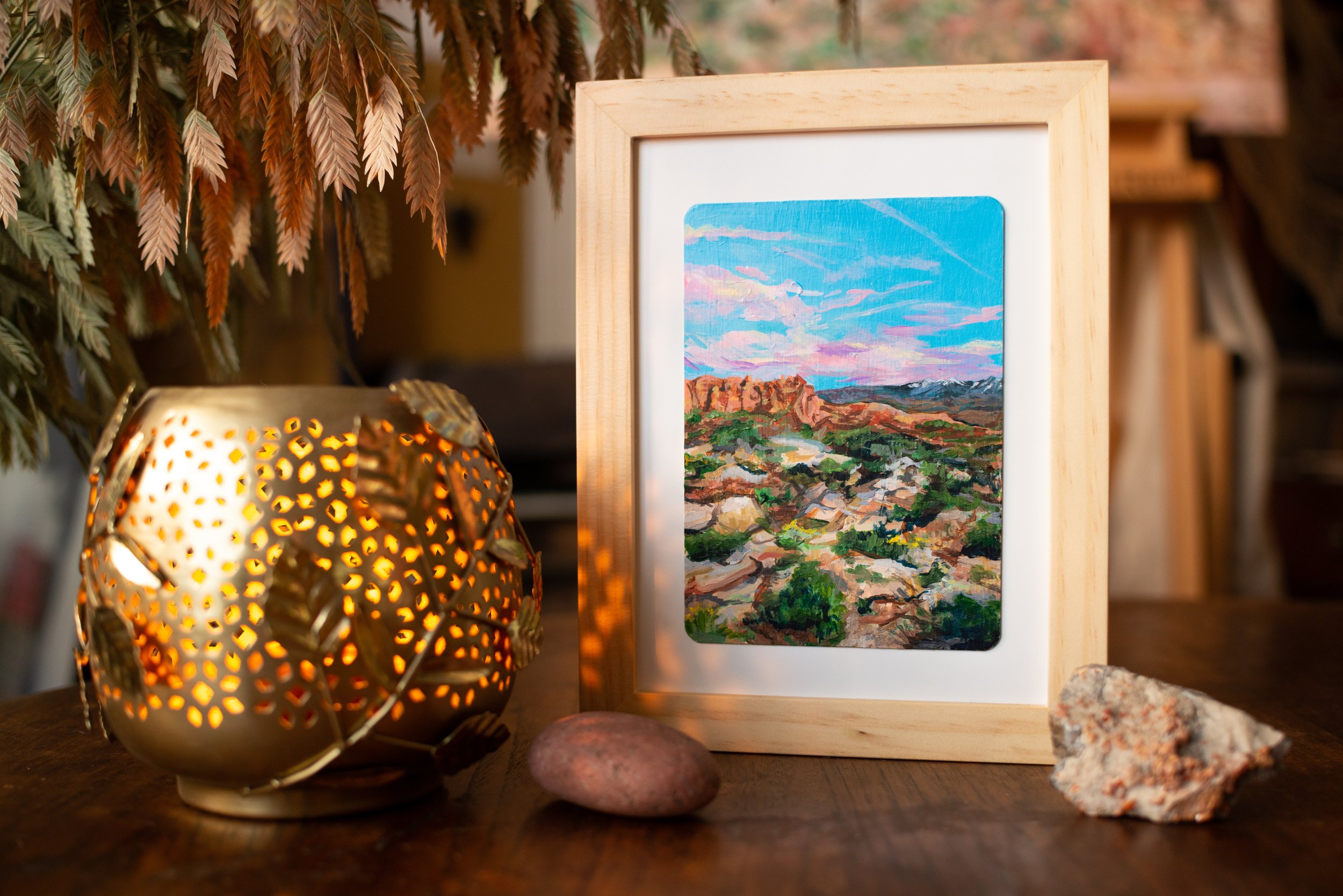 The original artwork framed on a table and styled rocks and a decorative candle holder around the frame.