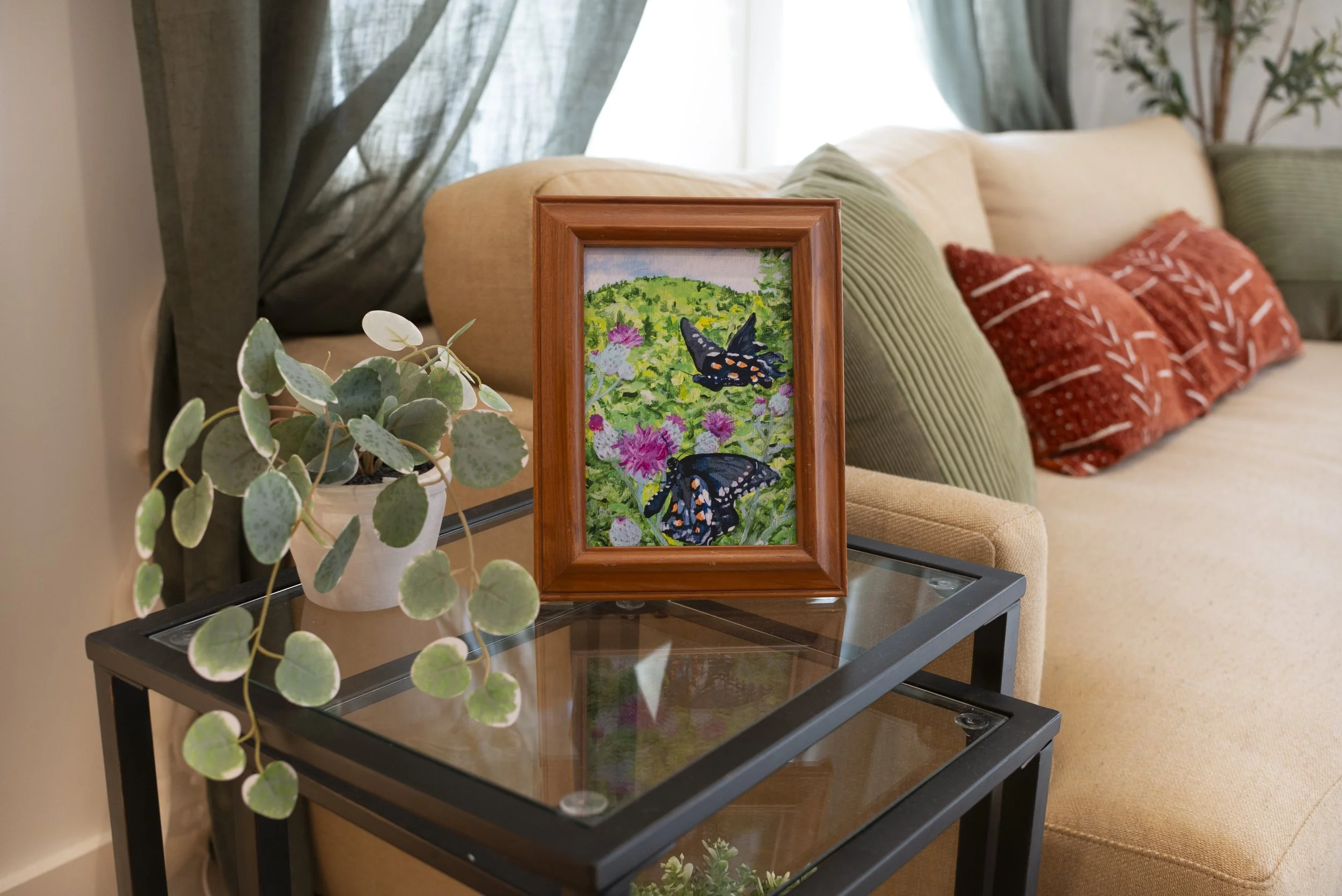 A framed Swallowtail butterflies art print on a side table in a living room in front of a couch.