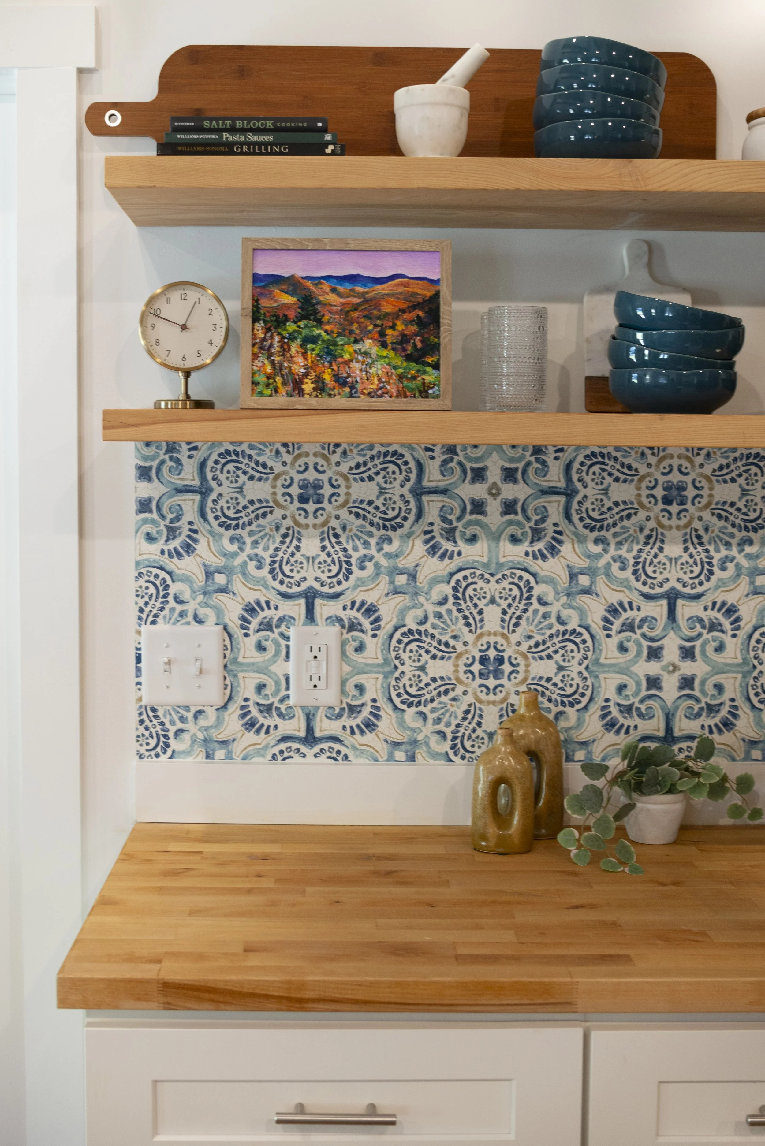 A framed print of a Blue Ridge Parkway overlook in the fall, displayed on a kitchen shelf in a cozy, modern kitchen with wooden shelves and colorful accents.