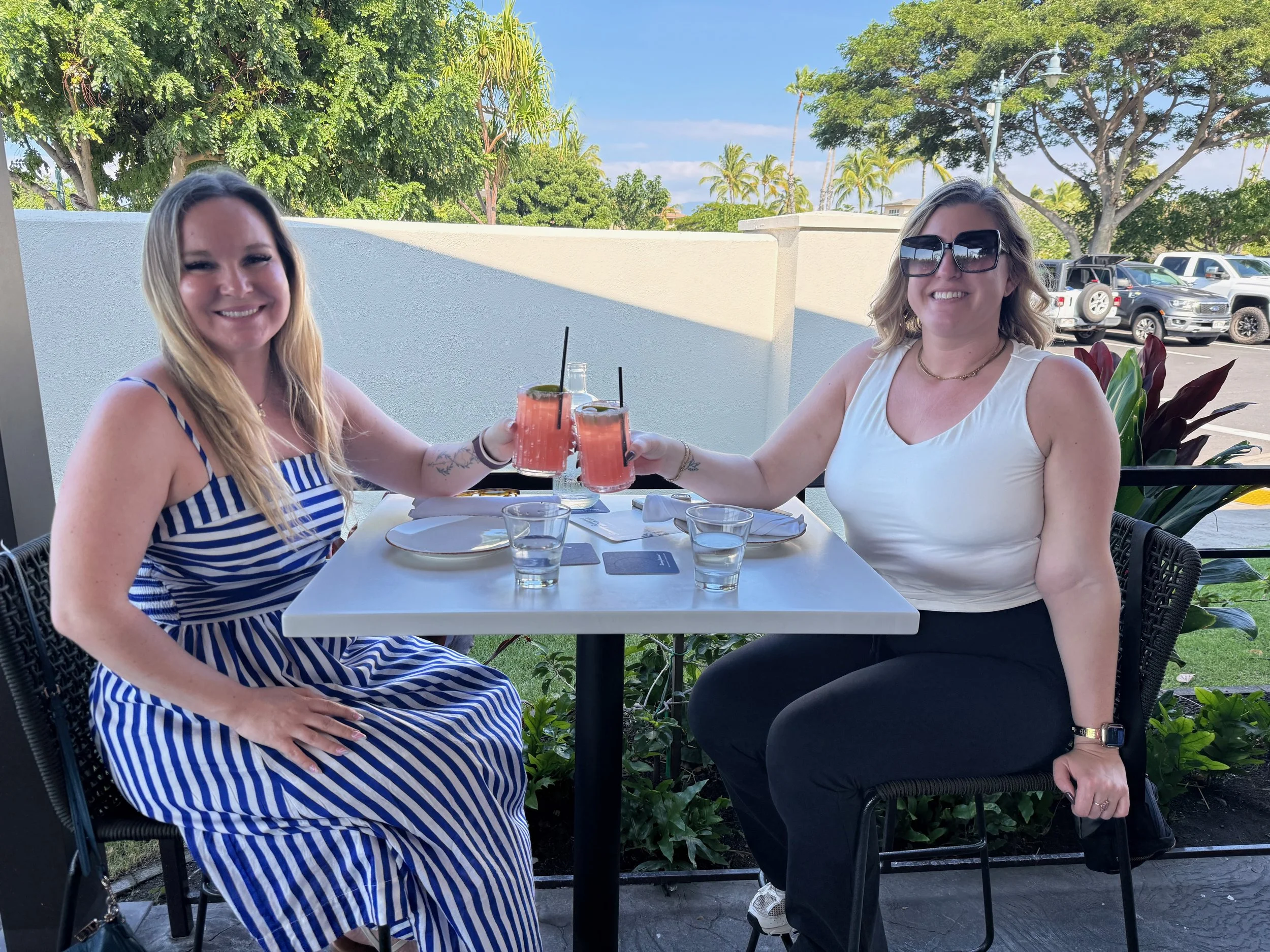 Two friends toasting cocktails on a sunny outdoor patio in Waimea, Hawaii
