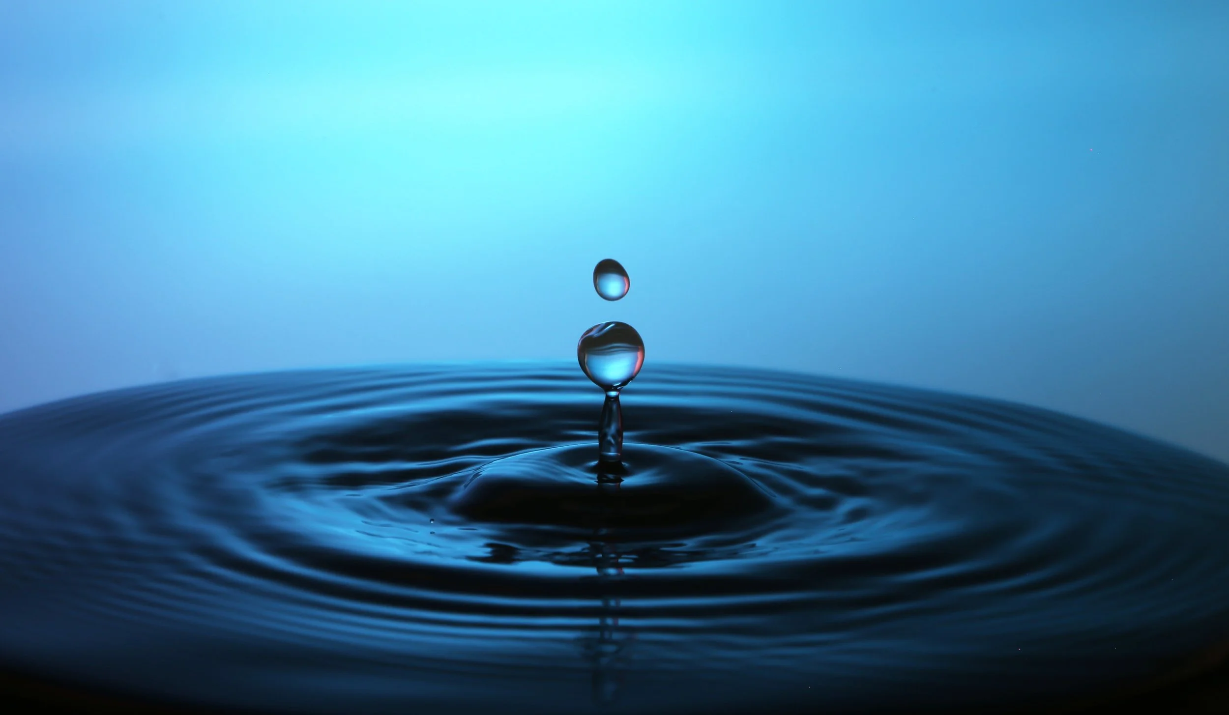 A close-up of a water droplet falling into a calm body of water, creating ripples and a splash.