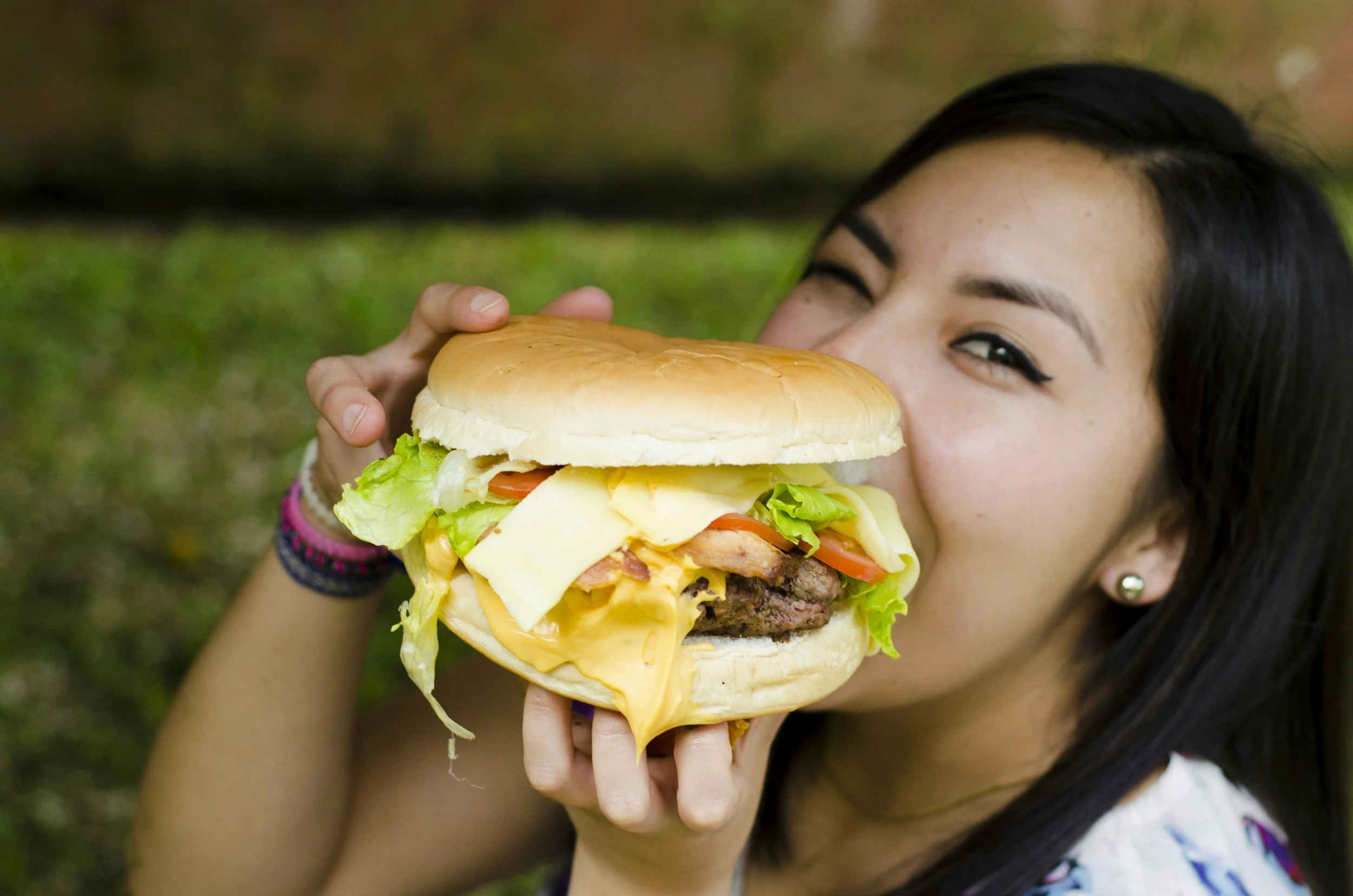 A girl with black hair and earrings holding a large cheeseburger.