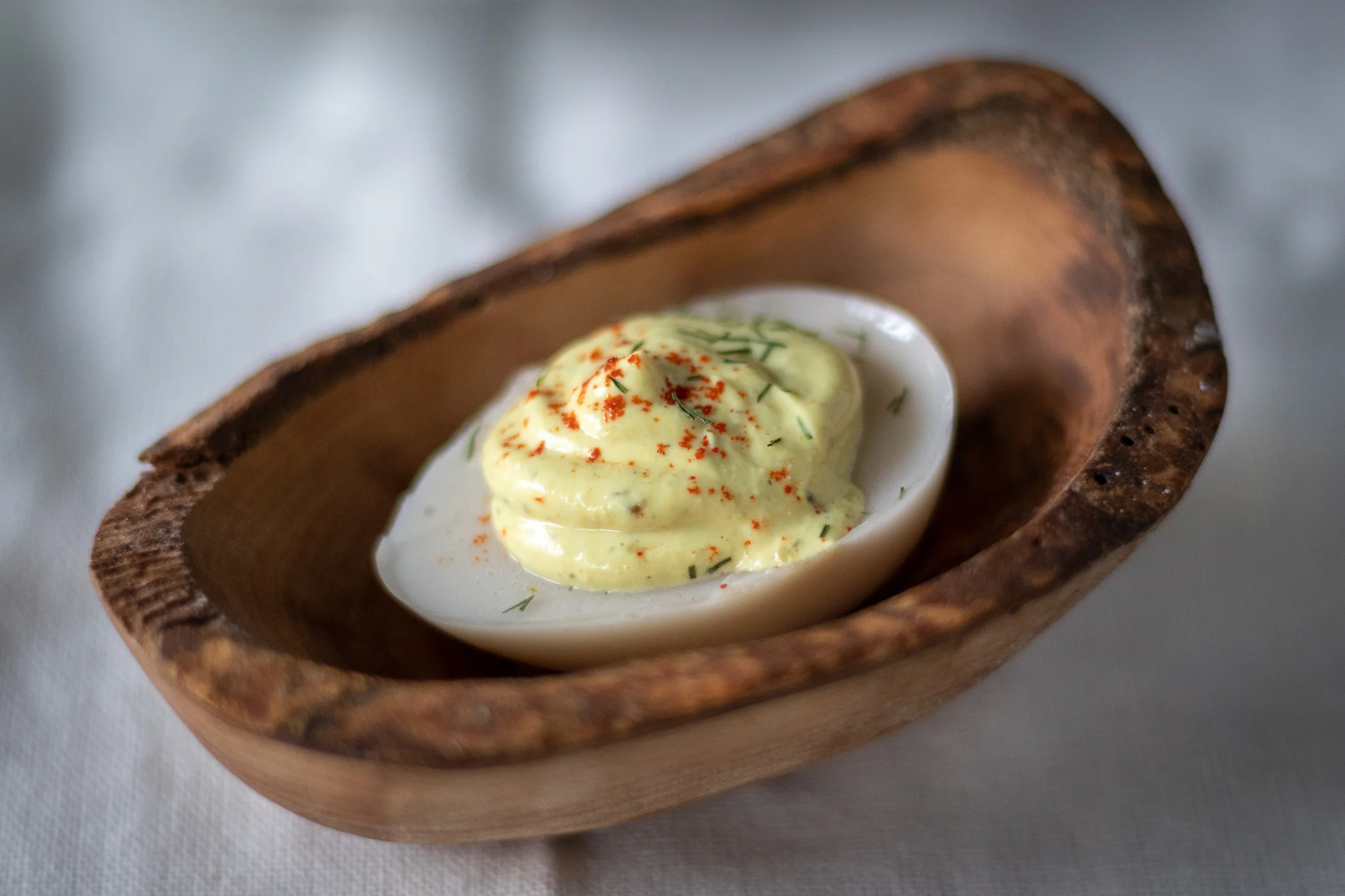 A single vegan deviled egg in a wooden serving dish