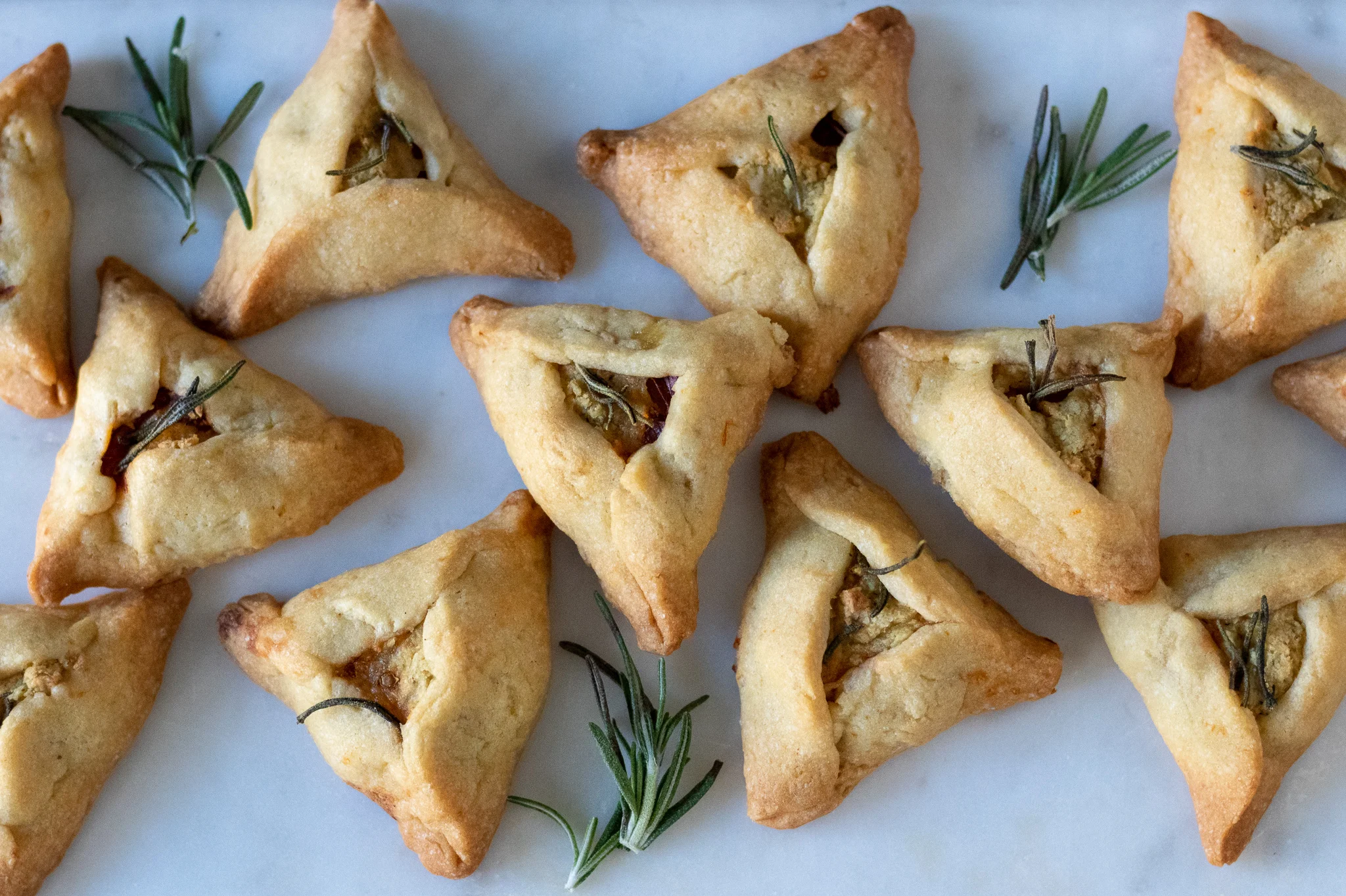 Meet the unsung hero of the Hamantaschen cookie! The savory Hamantaschen! Hamantaschen are made to celebrate the Jewish holiday of Purim, which celebrates the bravery of Esther against the evil, Haman. Although the cookies are typically sweet and filled with things like poppy seeds, jam, or chocolate, I decided this year to try a savory Hamantaschen using our alomond herb goat cheese , rosemary, and tomato. We left the dough a little sweet with a hint of lemon, but y'all, it works! Nobody in my house was booing these cookies. They are delicious! I did have some trouble at first convincing some friends to try these. After all, who makes savory Hamantaschen? But once I talked them into it, they were pleasantly surprised! So if you are ready to change up your regular Hamantaschen game, give these a go. Even if you have never heard of a Hamantaschen cookie, you don’t have to celebrate Purim to bake up a batch of these tasty treats! Vegan Hamantaschen for everyone!
